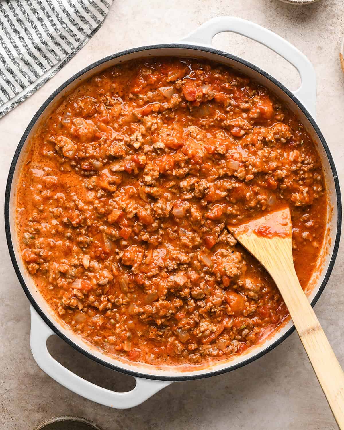 Making baked ziti - ingredients are in a white saucepan and being mixed together with a wooden spoon