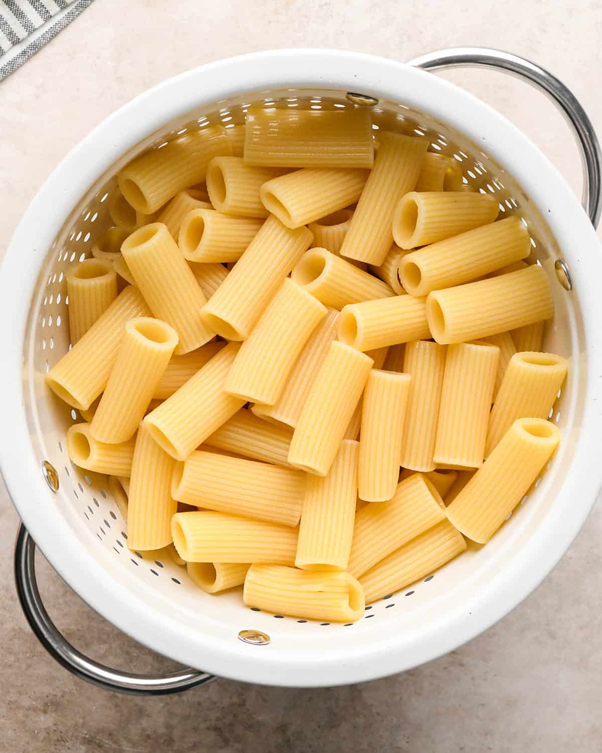 Cooked ziti pasta in a white colander sitting on a countertop.