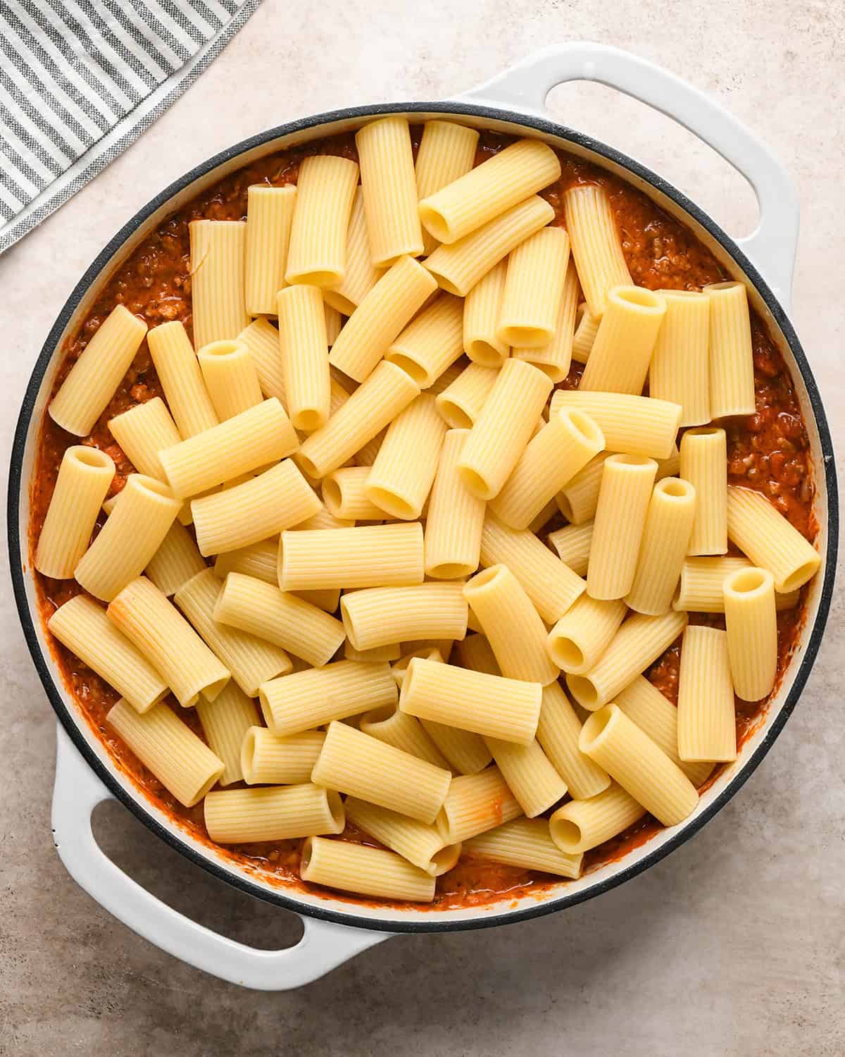 Making baked ziti - cooked ziti pasta is added to saucepan with the prepared sauce.