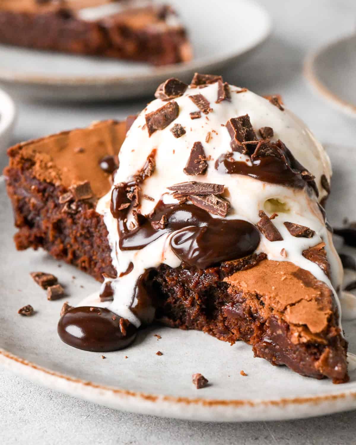 Close up photo of one slice of a cast iron skillet brownie topped with vanilla ice cream, chocolate sauce, and chocolate shavings and served on a white plate