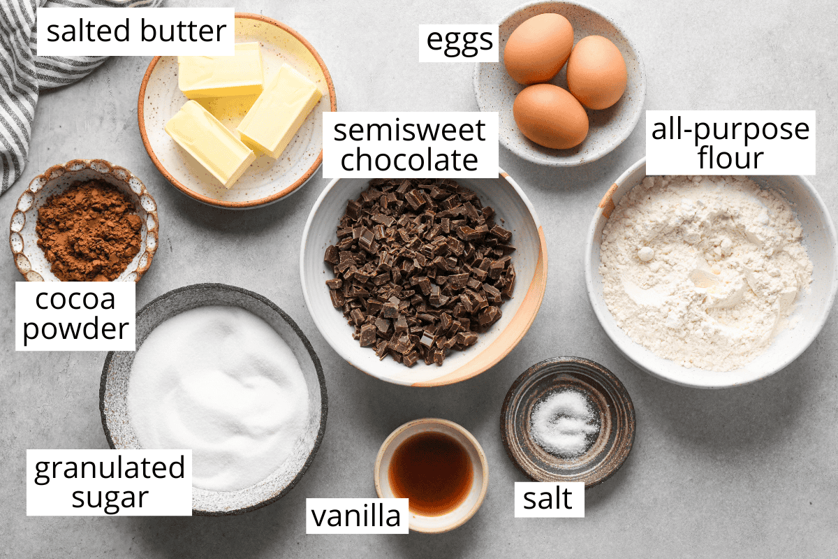 Overhead description of the labeled ingredients in this skillet brownie recipe like cocoa powder, sugar, semisweet chocolate, vanilla, salt, butter, eggs, and all-purpose flour