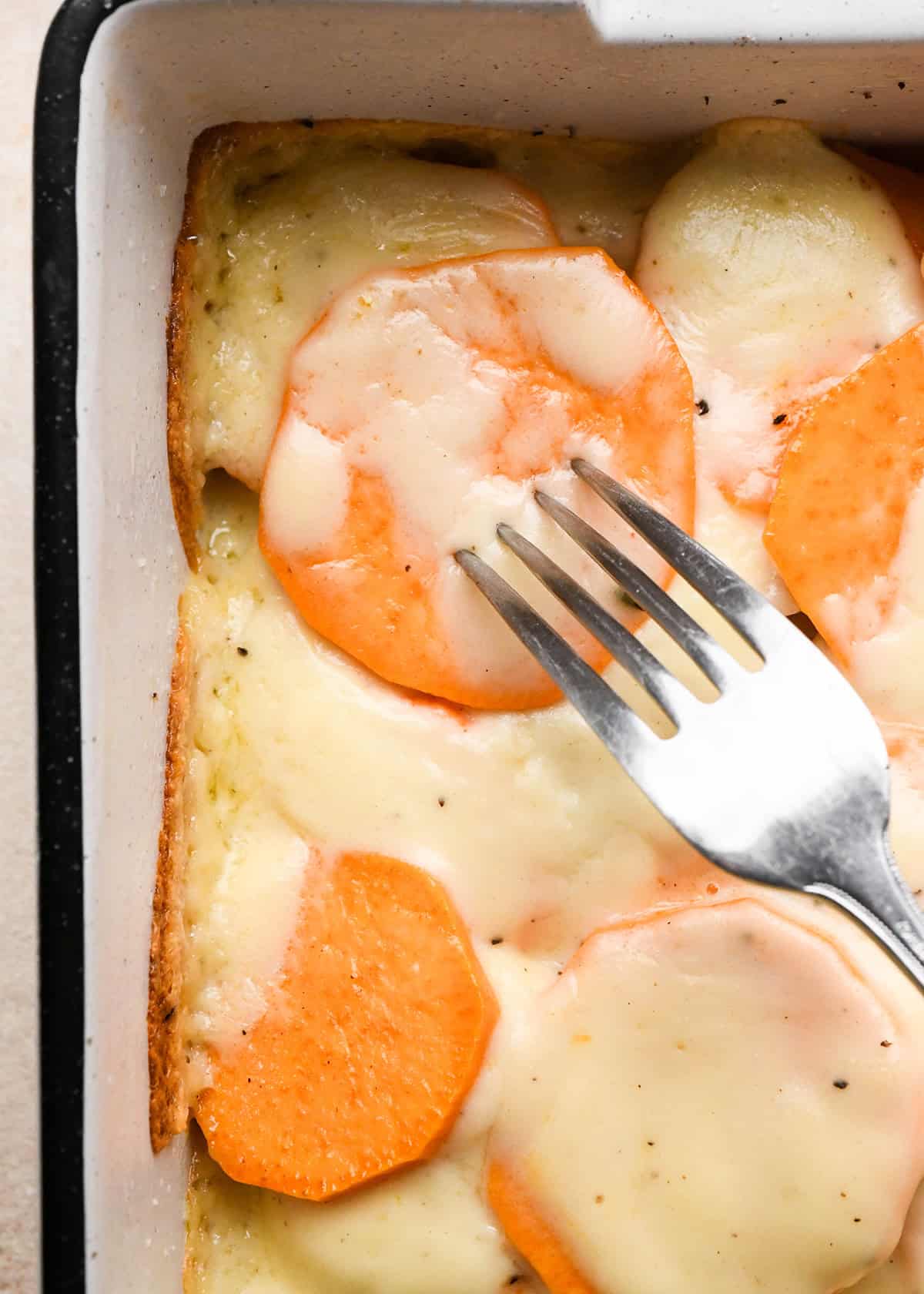 making sweet potato gratin - a fork inserted into a sweet potato showing it's soft during baking