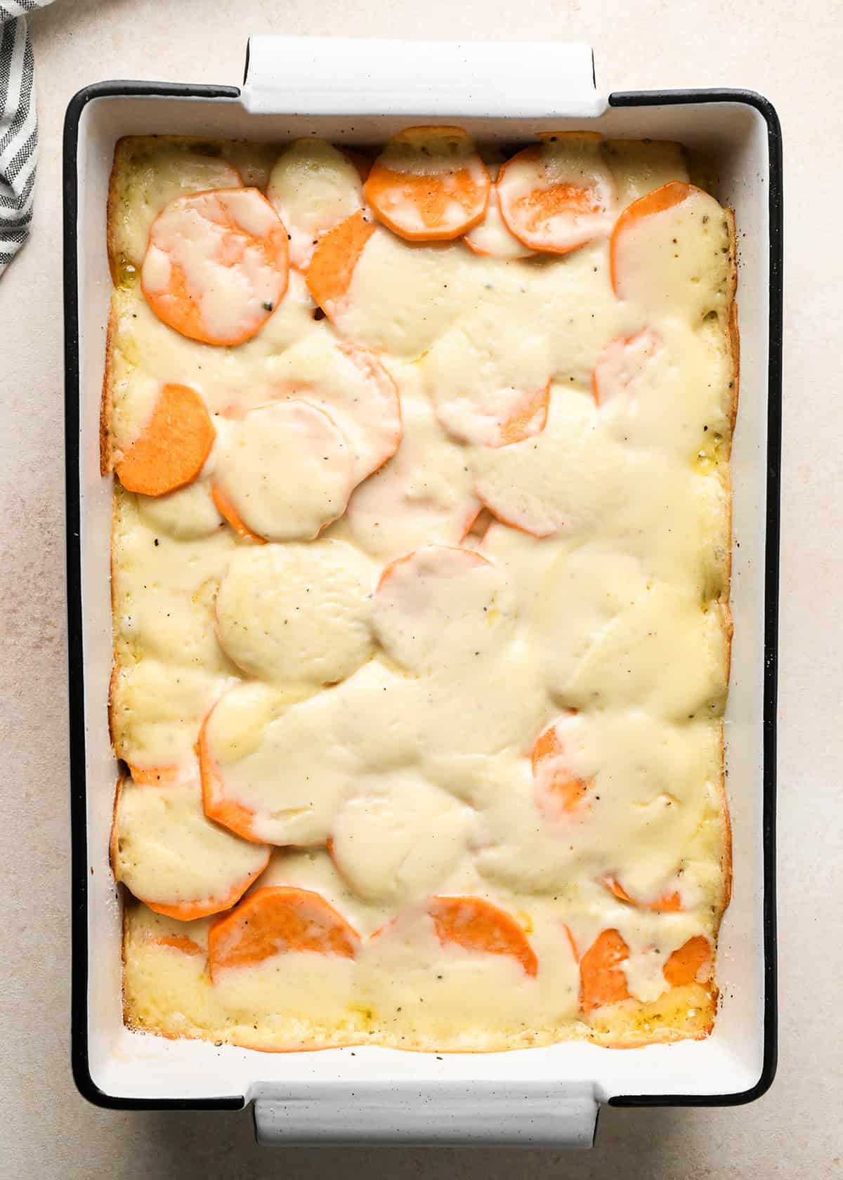partially baked sweet potato gratin in a white baking dish with a black rim
