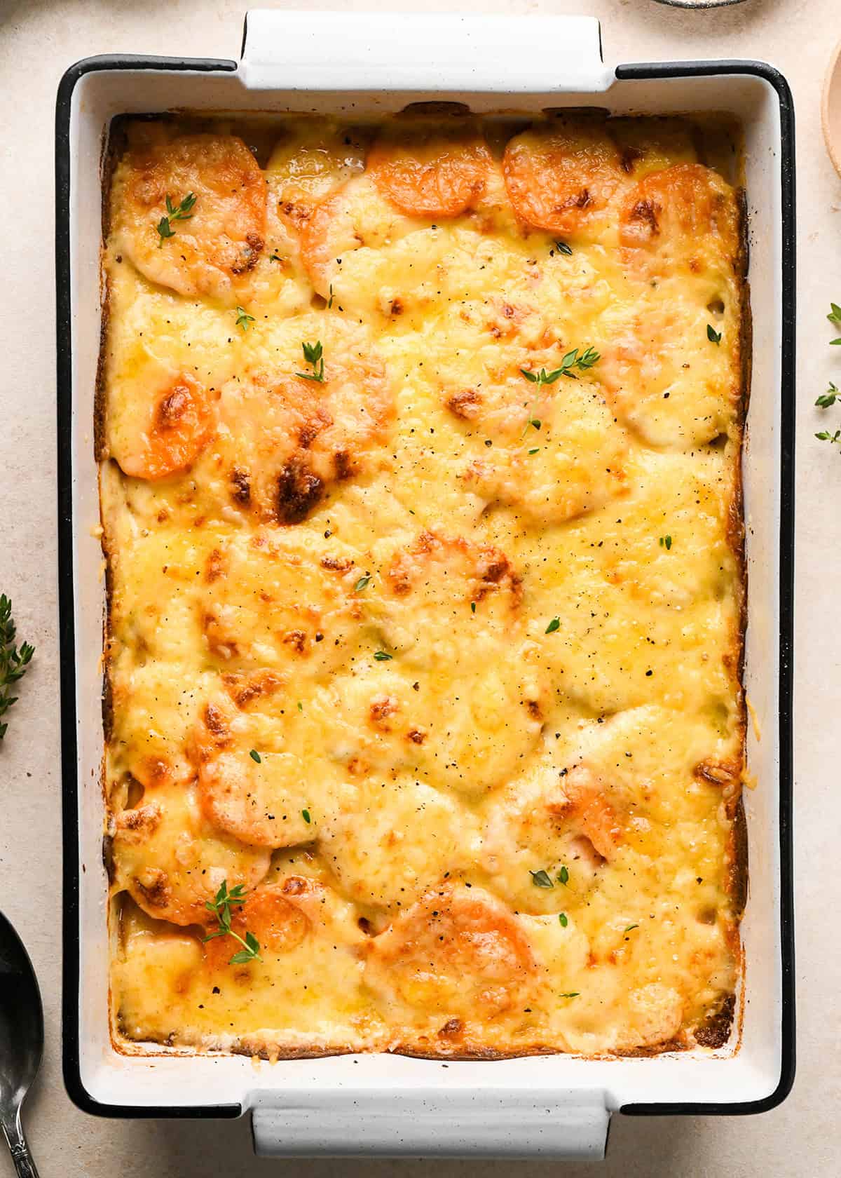 sweet potato gratin in a baking dish after baking  topped with melted cheese, fresh thyme and black pepper