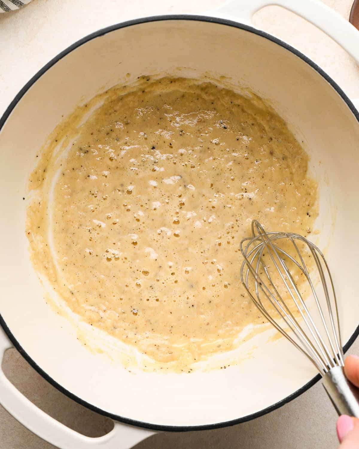 making sweet potato gratin - the roux cooking and being stirred with a whisk in a white pot