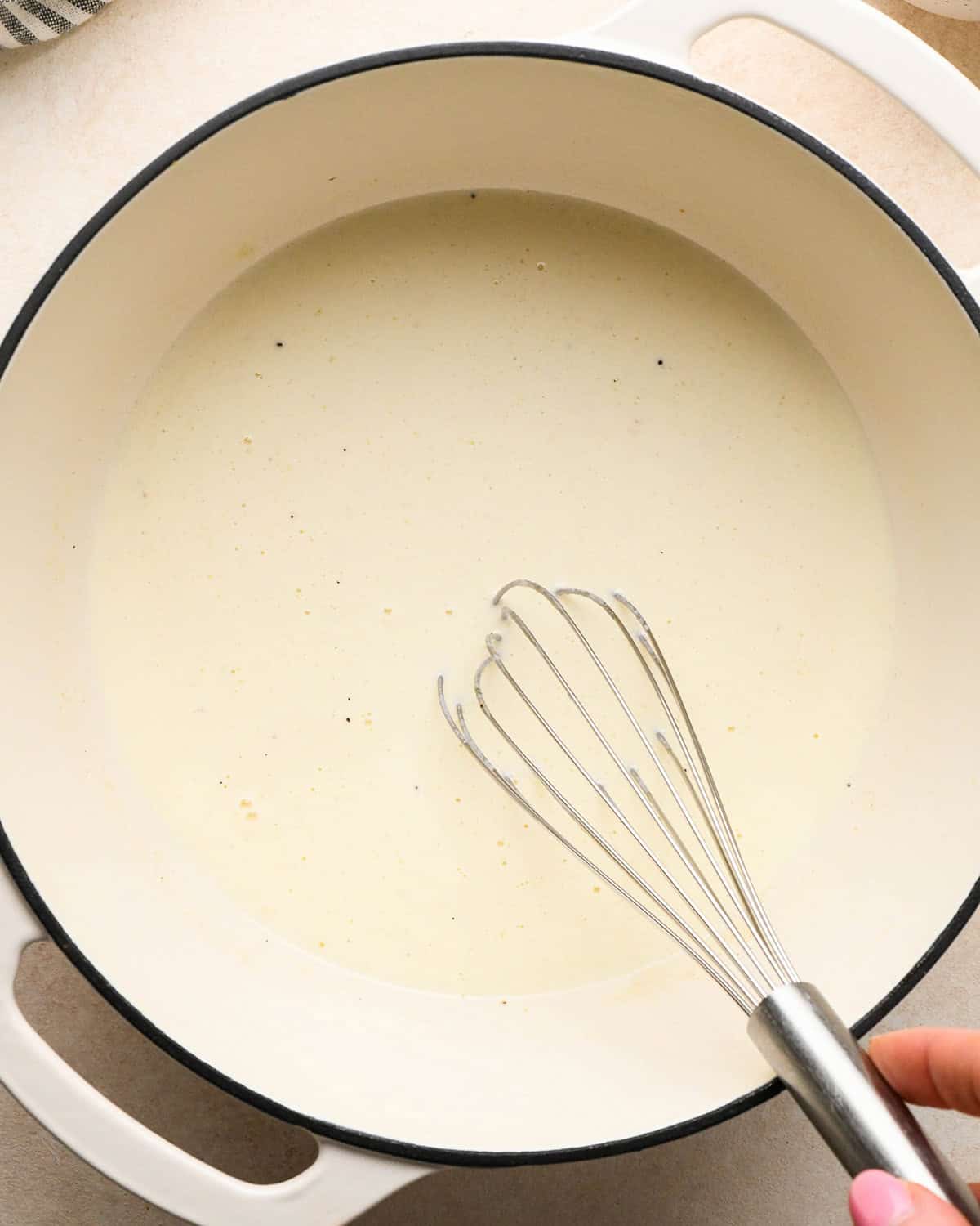 making sweet potato gratin - a whisk in a white pot mixing the cheese sauce