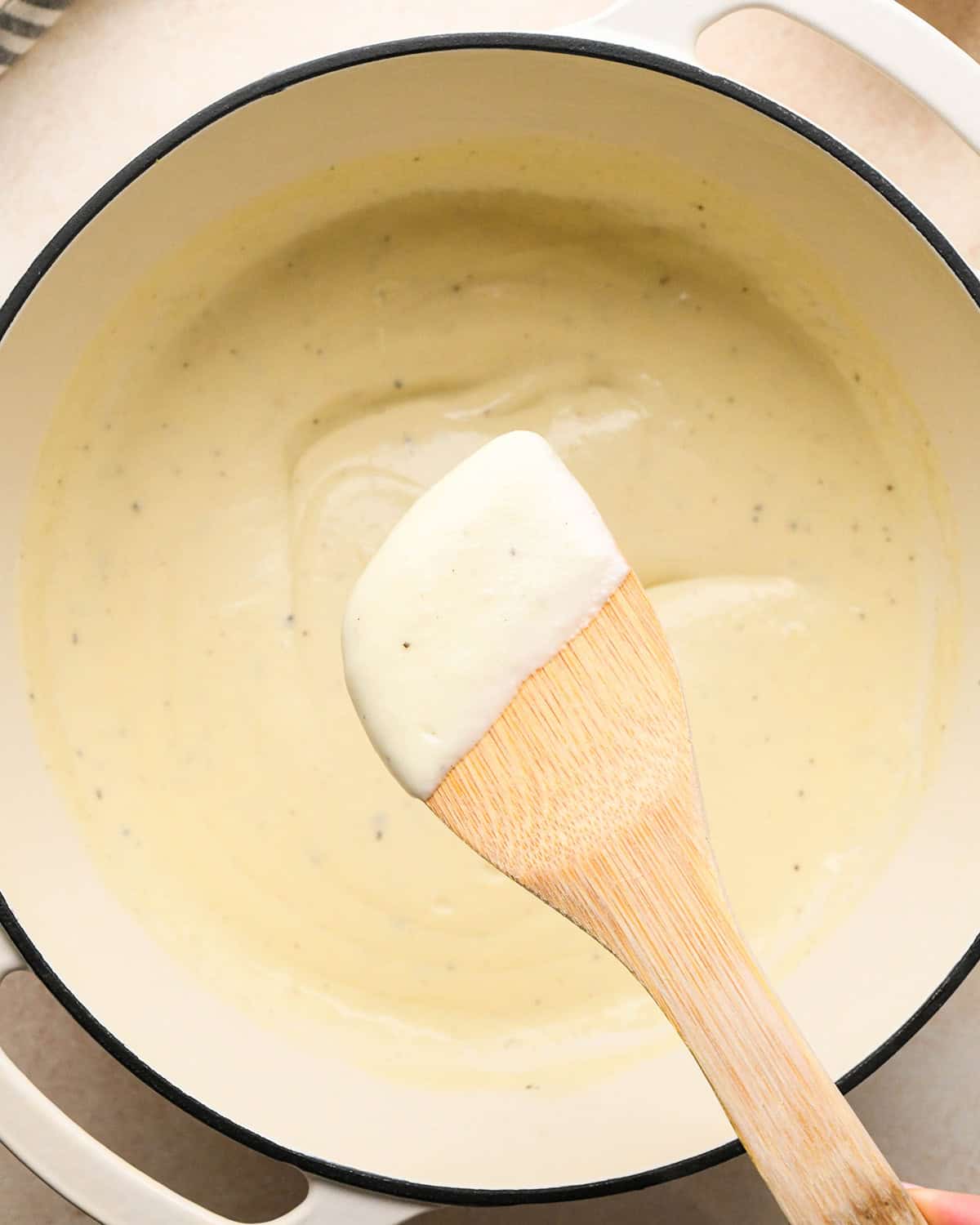 making sweet potato gratin - a wooden spatula showing the thickened cheese sauce 