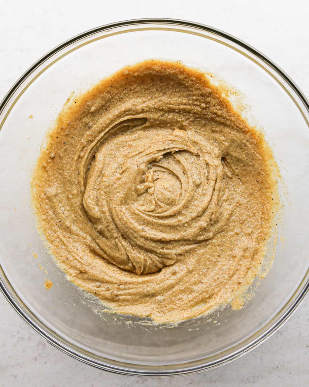 Making brown butter oatmeal cookies - overhead photo of an egg and vanilla being mixed into cookie dough in a clear bowl.