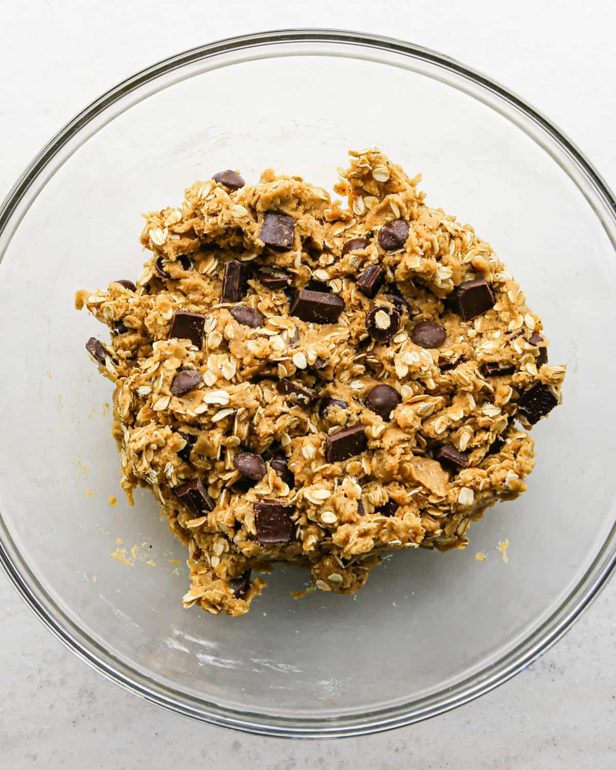 Making brown butter oatmeal cookies - overhead photo of oats, chocolate chips, and chocolate chunks mixed into cookie dough in a clear bowl.