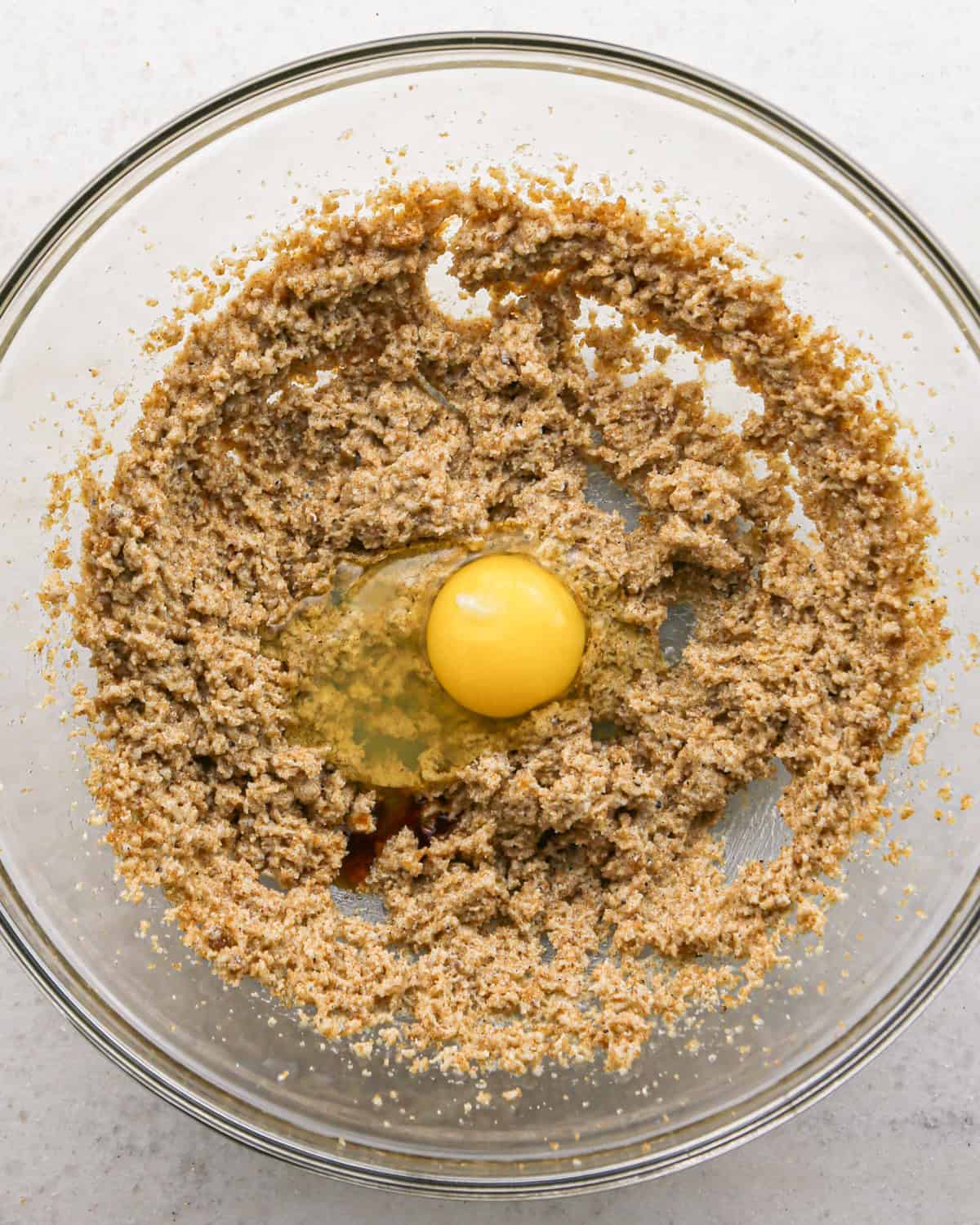 Making brown butter oatmeal cookies - overhead photo of an egg and vanilla being added to cookie dough in a clear bowl.
