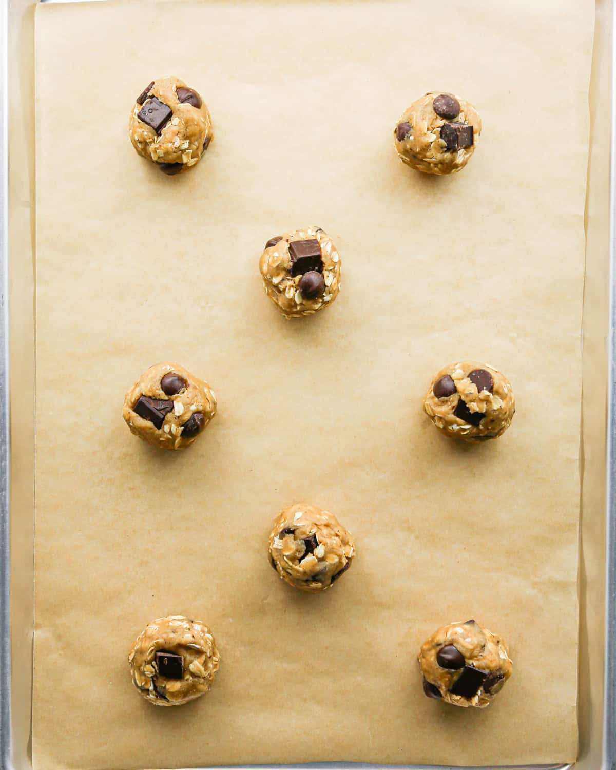 Making brown butter oatmeal cookies - overhead photo of 8 balls of cookie dough, sprinkled with flaky sea salt and placed on a baking sheet with parchment paper.