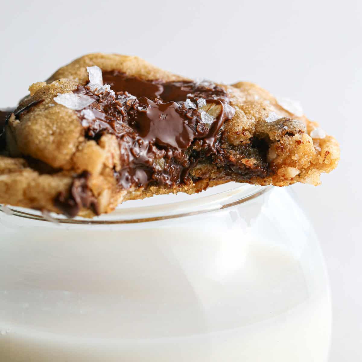 Close-up photo of 1 brown butter oatmeal cookie with a bite taken out of it and sitting on top of a glass of milk.