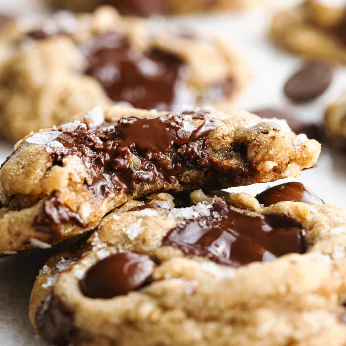 Close-up photo of brown butter oatmeal cookies with melted chocolate chunks and a sprinkle of flaky sea salt on top, with a bite taken out of the top cookie.
