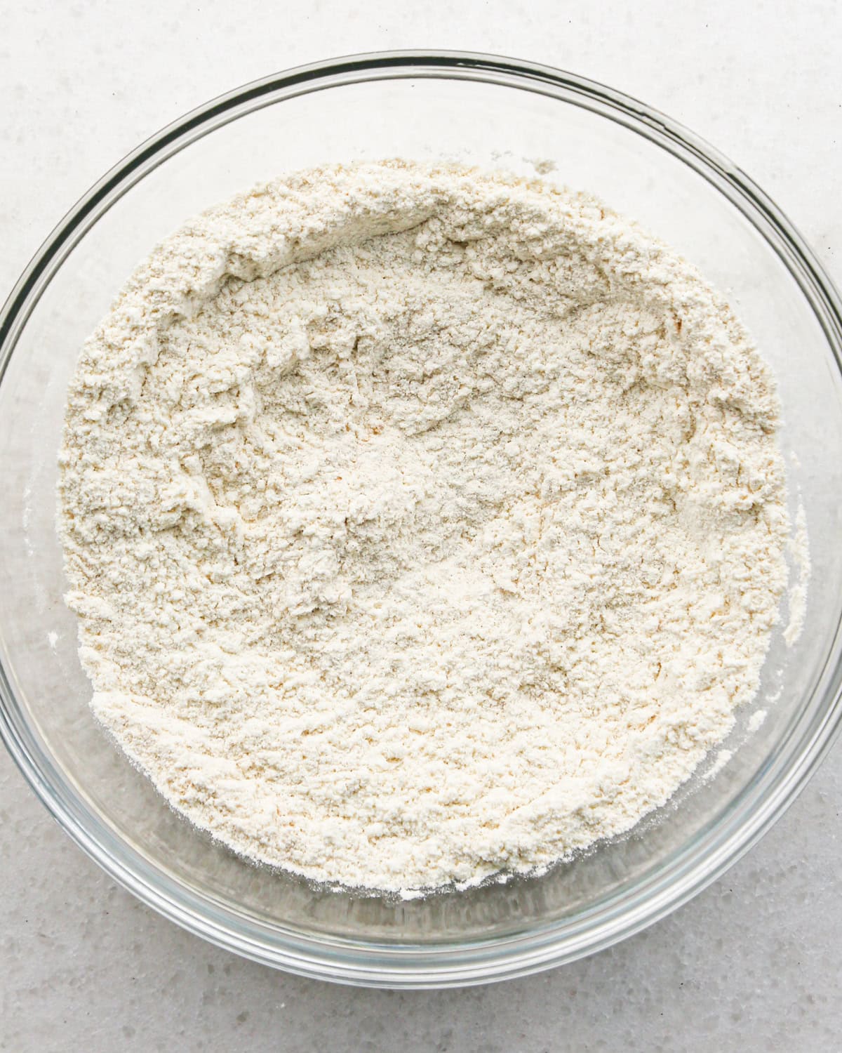 Making brown butter oatmeal cookies - overhead photo of dry ingredients being added to a clear mixing bowl and mixed together.