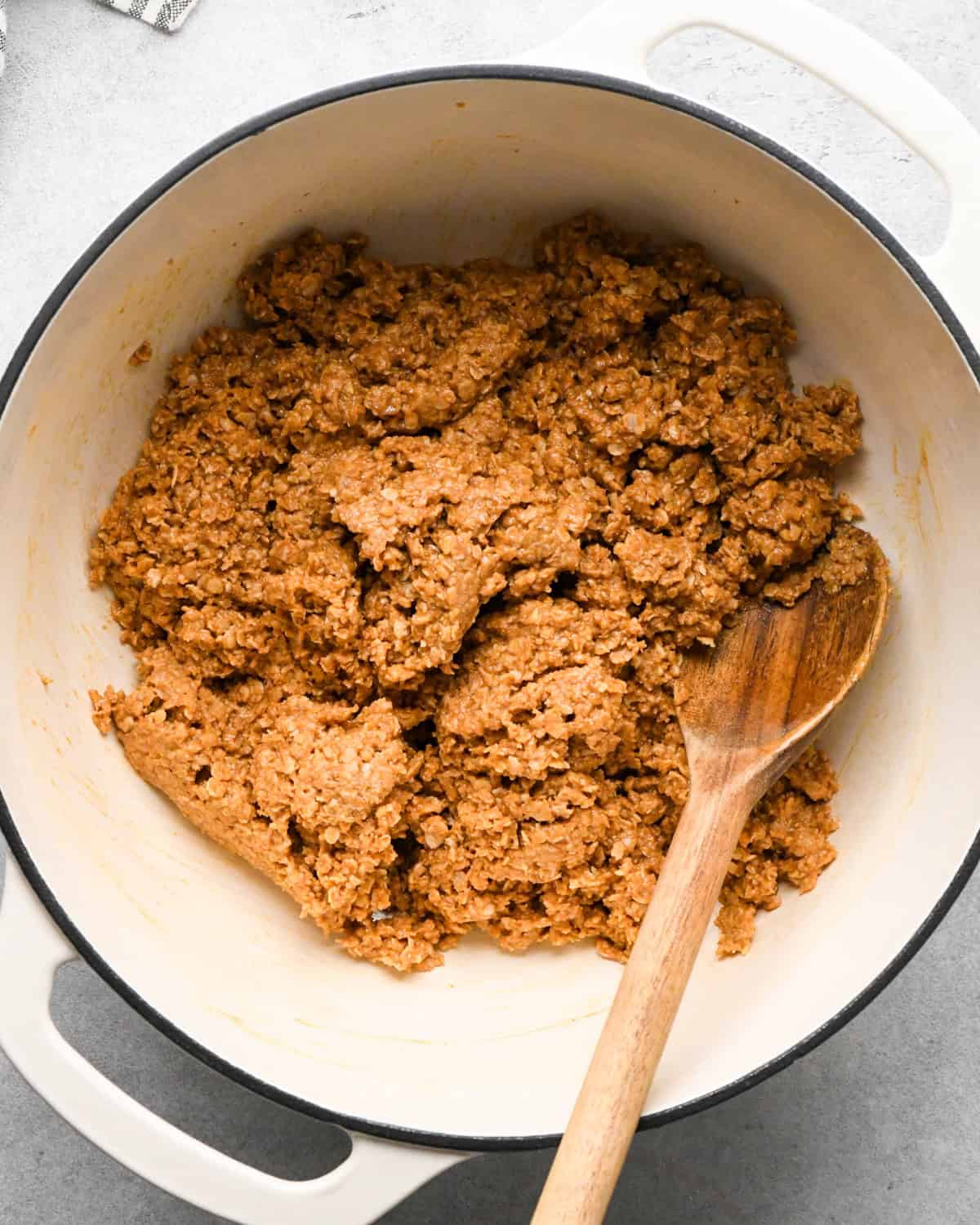 Making peanut butter oatmeal bars - overhead photo of quick-cooking oats being added to wet ingredients and mixed together with a wooden spoon.