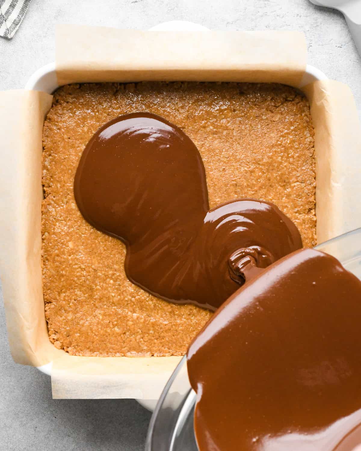 Making peanut butter oatmeal bars - overhead photo of melted peanut butter and chocolate being poured over peanut butter oatmeal bars mixture.