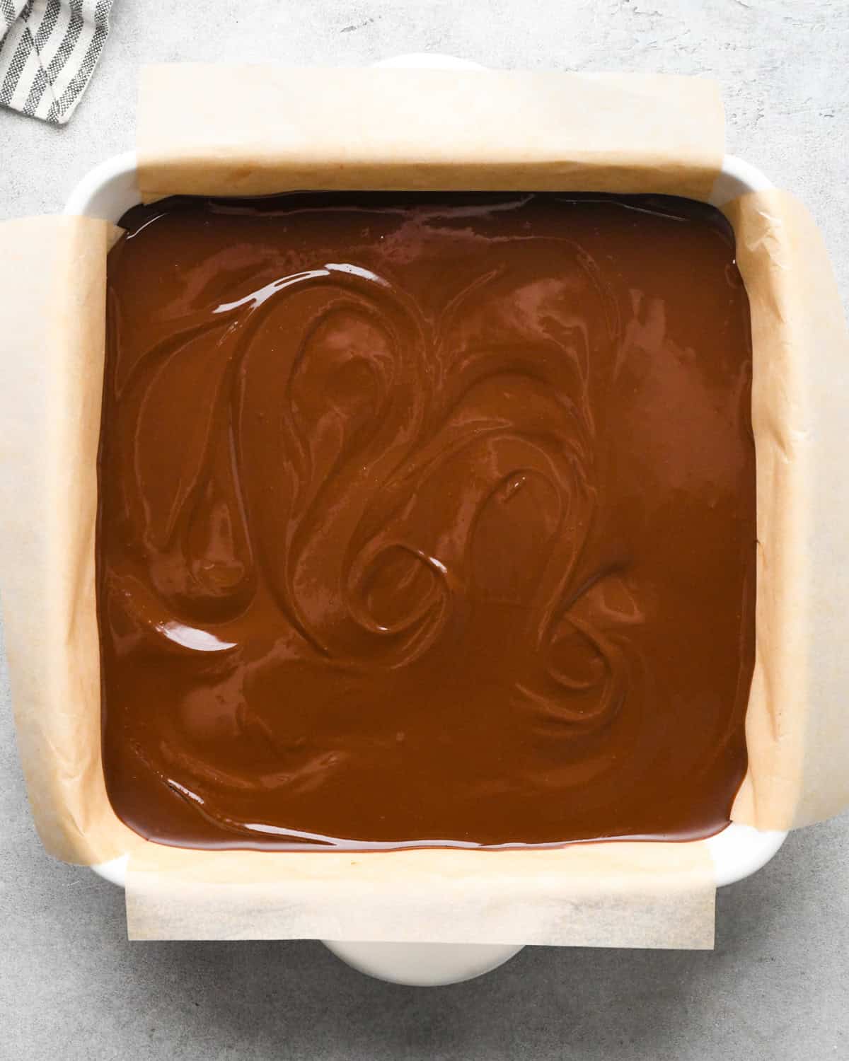 Peanut butter oatmeal bars topped with melted peanut butter and chocolate in a parchment-paper-lined casserole dish.