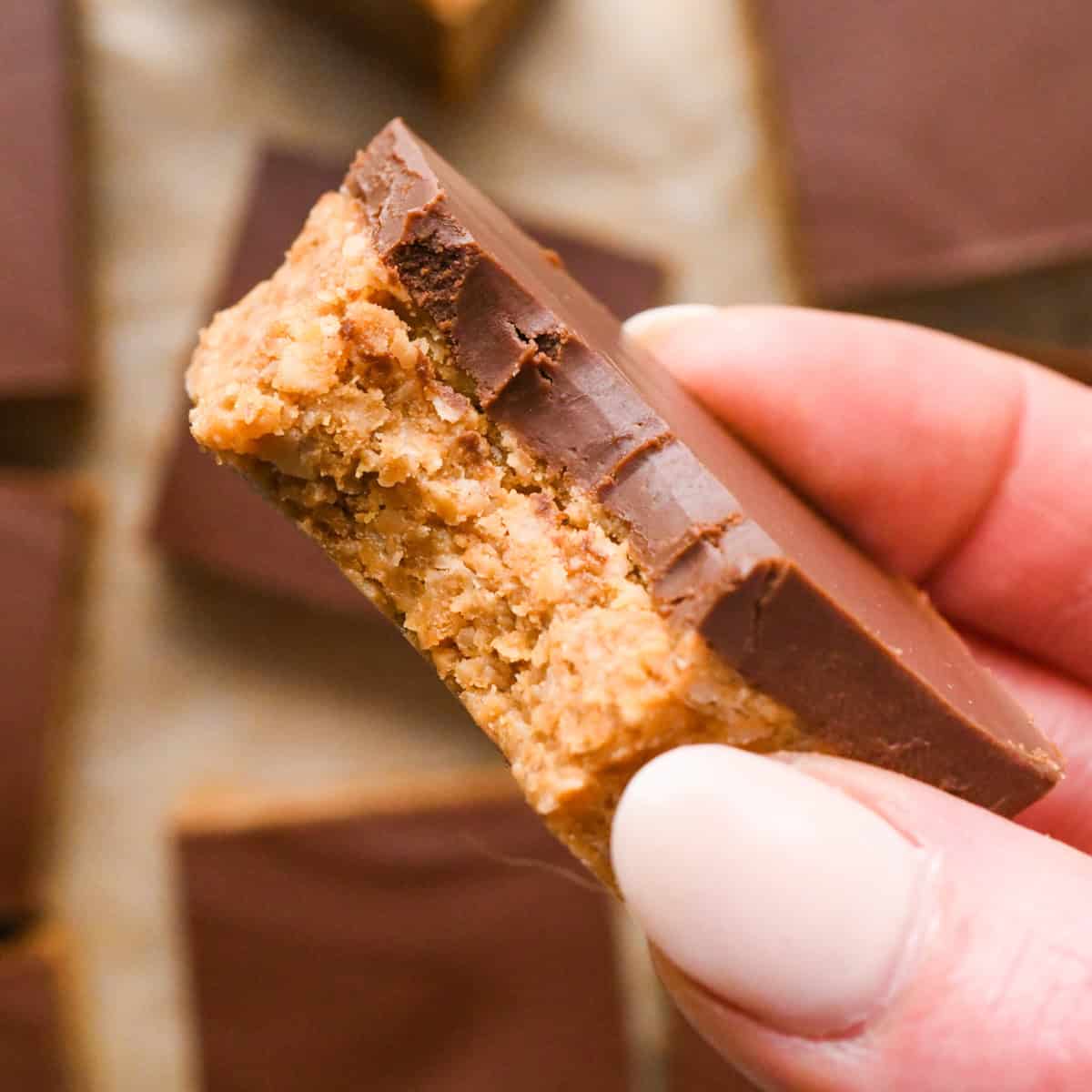 Overhead photo of a person holding one peanut butter oatmeal bar with a chocolate peanut butter topping, one bite is taken out of the square.