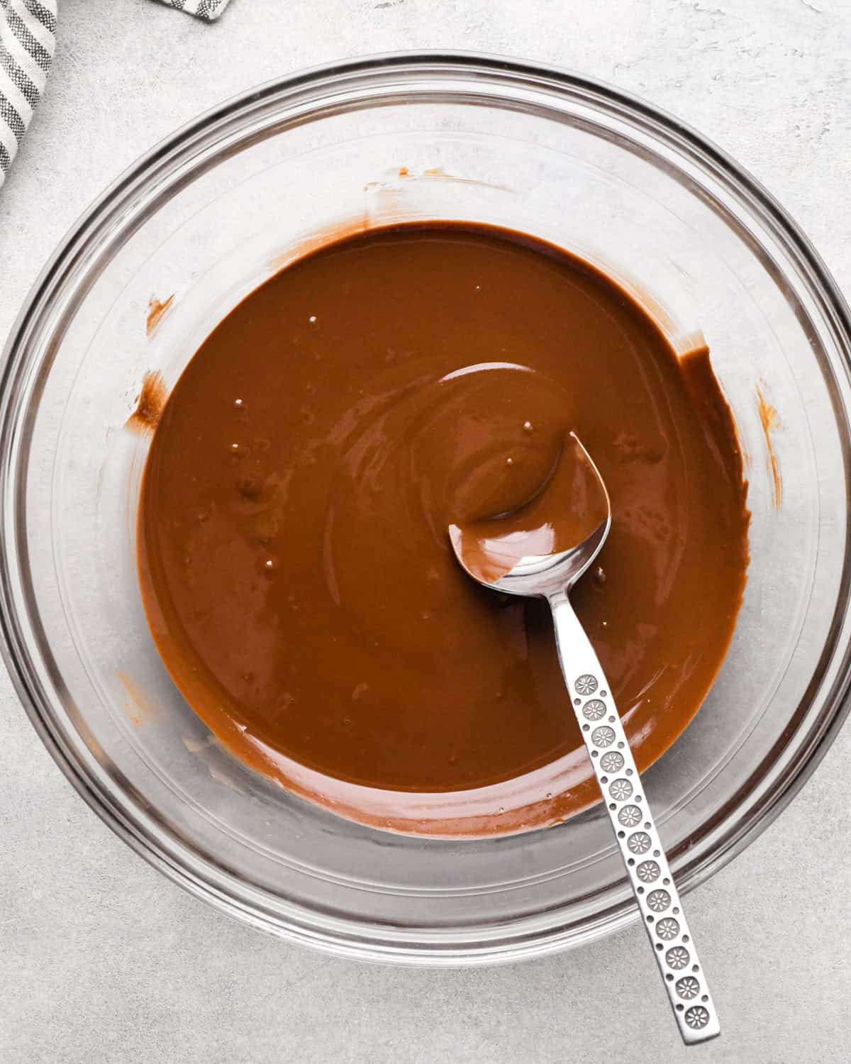 Making peanut butter oatmeal bars - overhead photo of peanut butter and semisweet chocolate chips melted together in a clear mixing bowl and being stirred with a silver spoon.