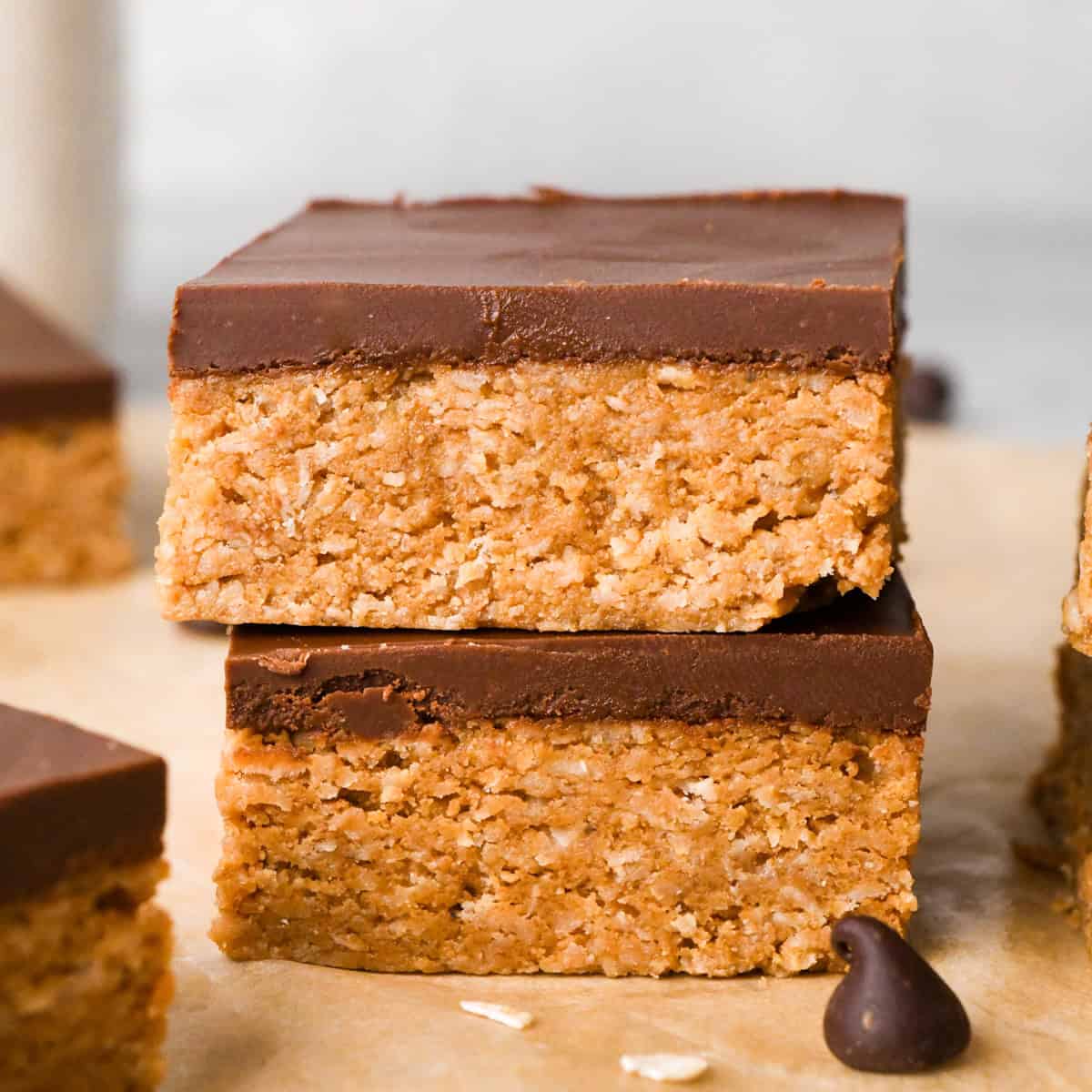 Close-up image of 2 peanut butter oatmeal bars topped with a smooth layer of chocolate and sitting on parchment paper.
