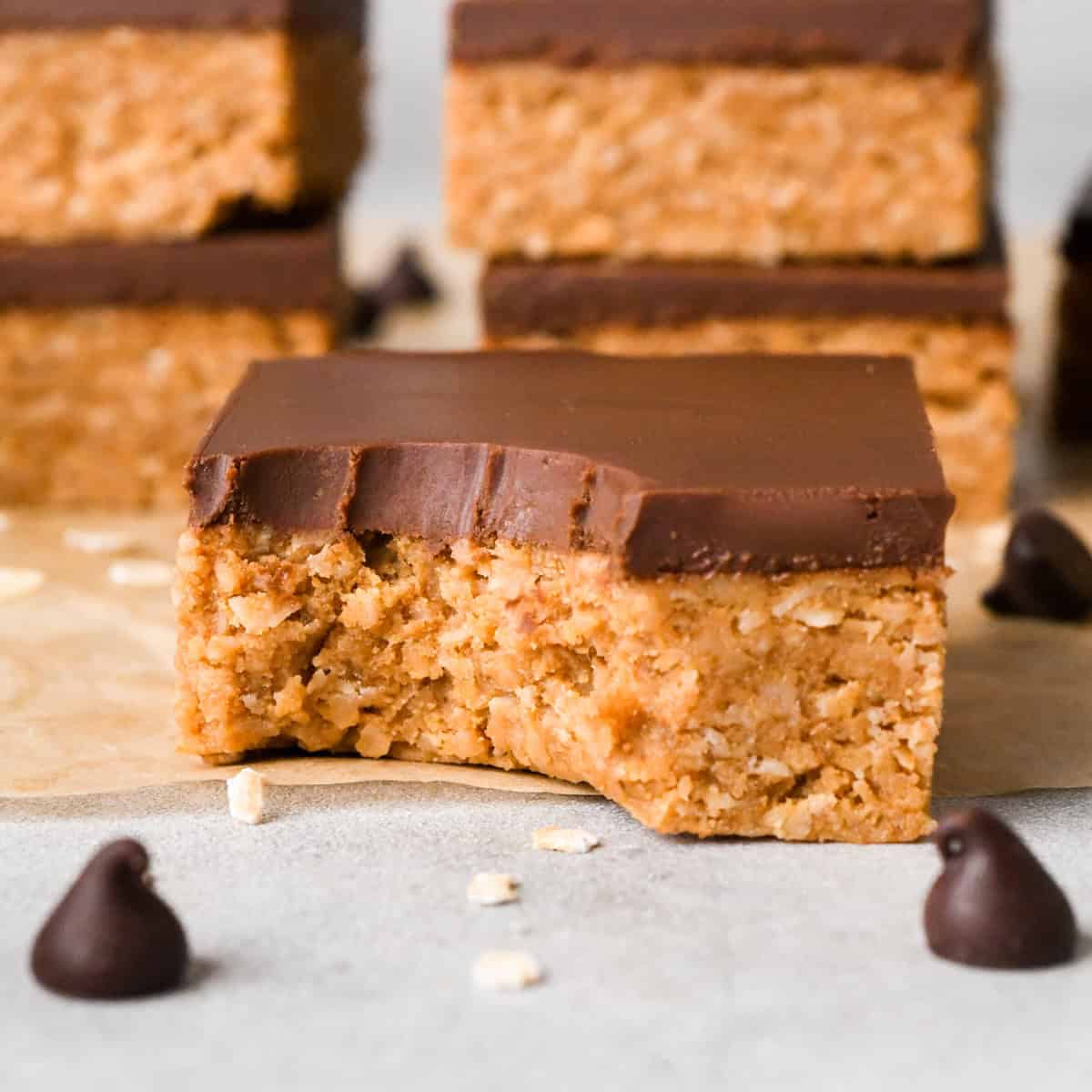 Close-up photo of a peanut butter oatmeal bar, topped with chocolate and with one bite taken out of it.
