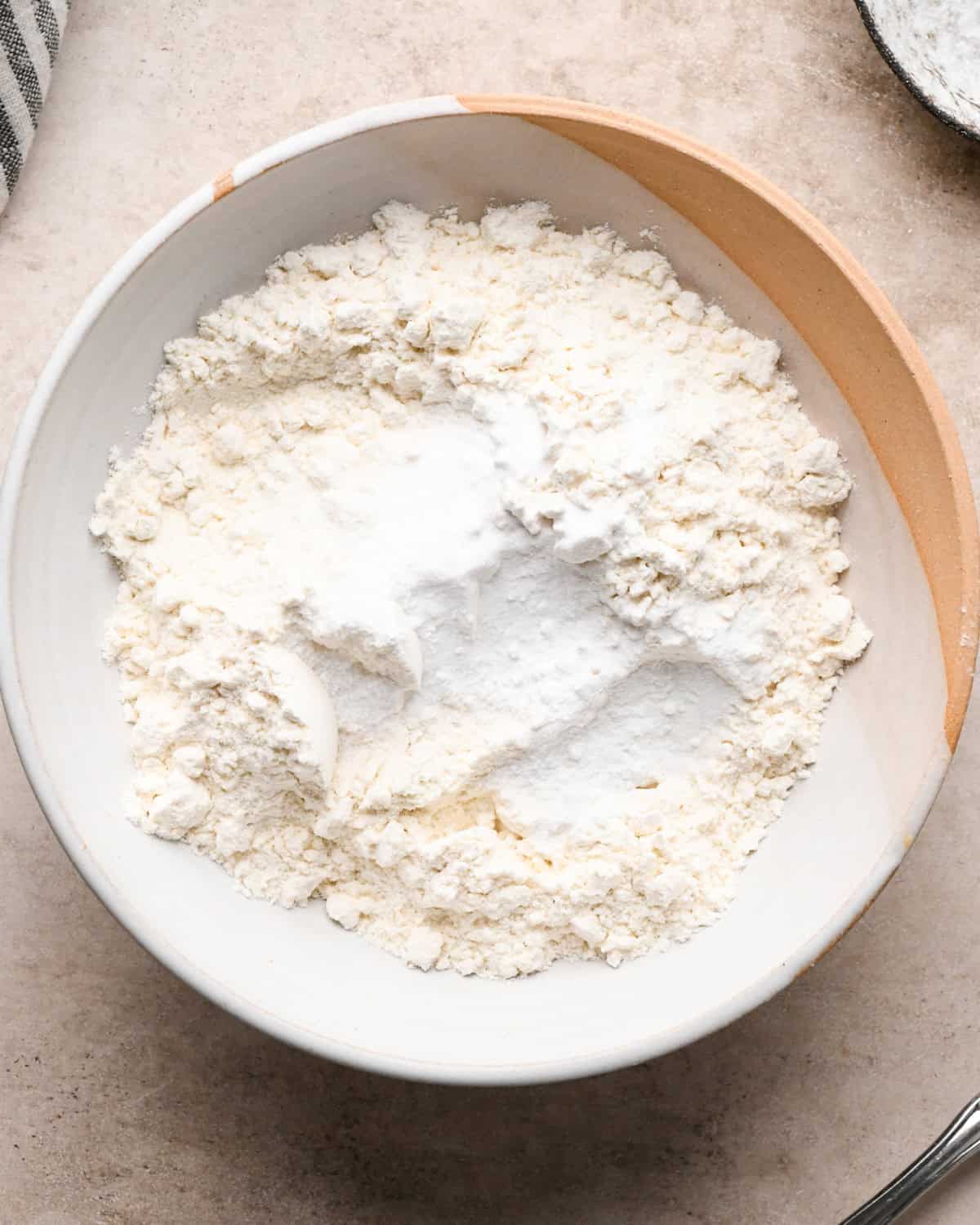 Making kitchen sink cookies - overhead photo of dry ingredients being added to a white-and-orange mixing bowl.