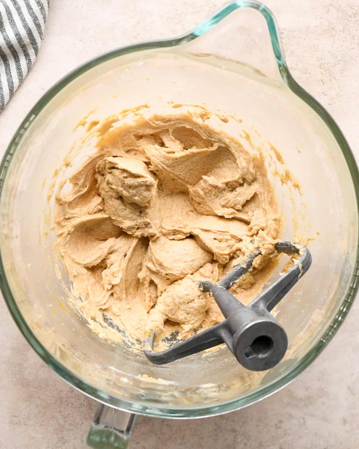 Making kitchen sink cookies - overhead photo of butter, sugar, brown sugar, egg, and vanilla in a clear measuring bowl, mixed together with a mixing bowl attachment.