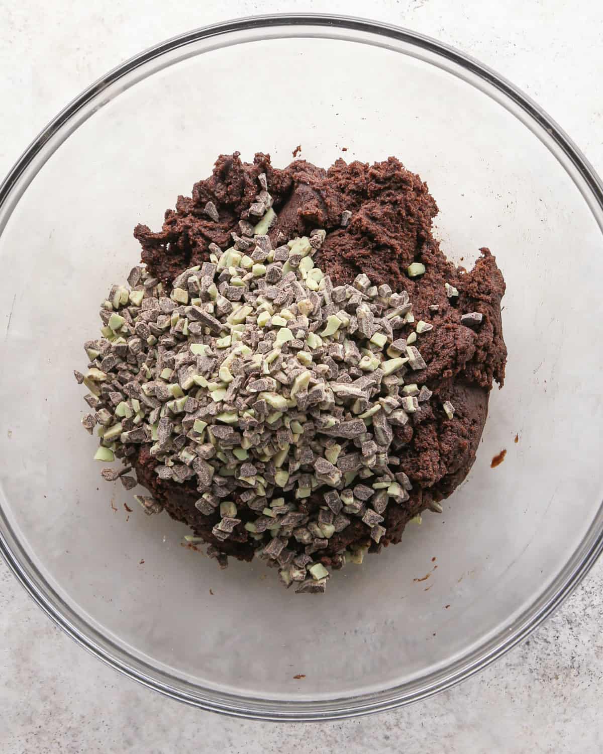 Making chocolate mint cookies - overhead photo of mint baking chips being added to cookie dough in a clear bowl.
