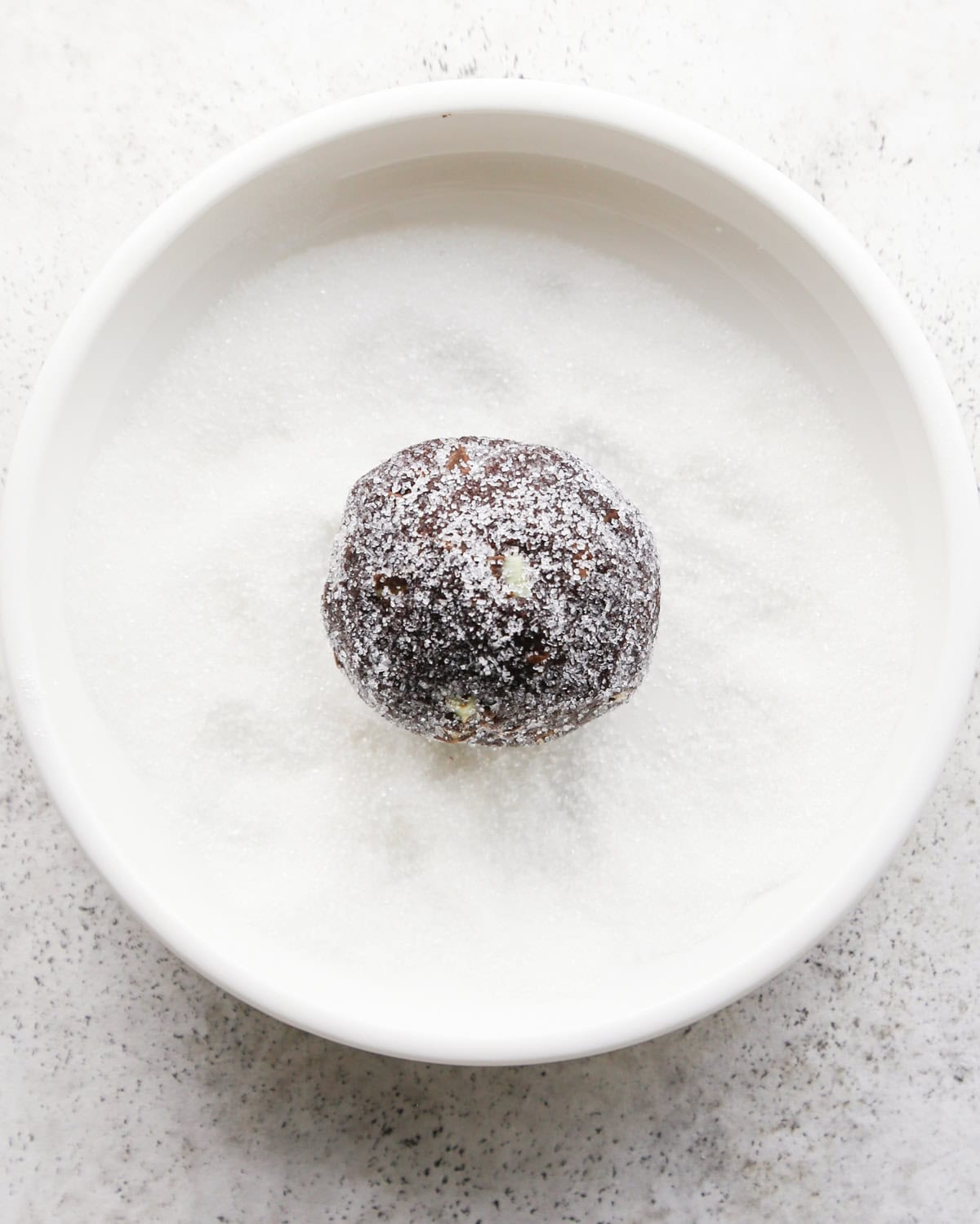 Making chocolate mint cookies - overhead photo of a ball of cookie dough being rolled in a bowl of sugar for coating.