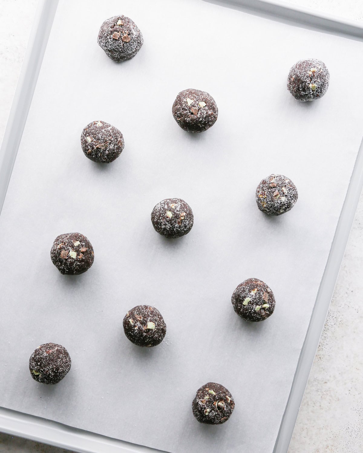 Making chocolate mint cookies - overhead photo of 11 chocolate mint cookie dough balls rolled in sugar and placed on a parchment-paper-covered baking sheet.