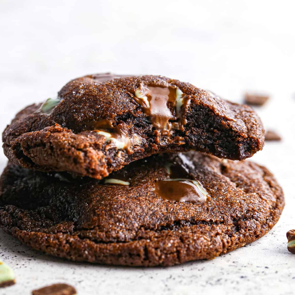 Close-up photo of 2 chocolate mint cookies stacked on top of each other with a bite taken out of the top cookie to show its soft and gooey texture.