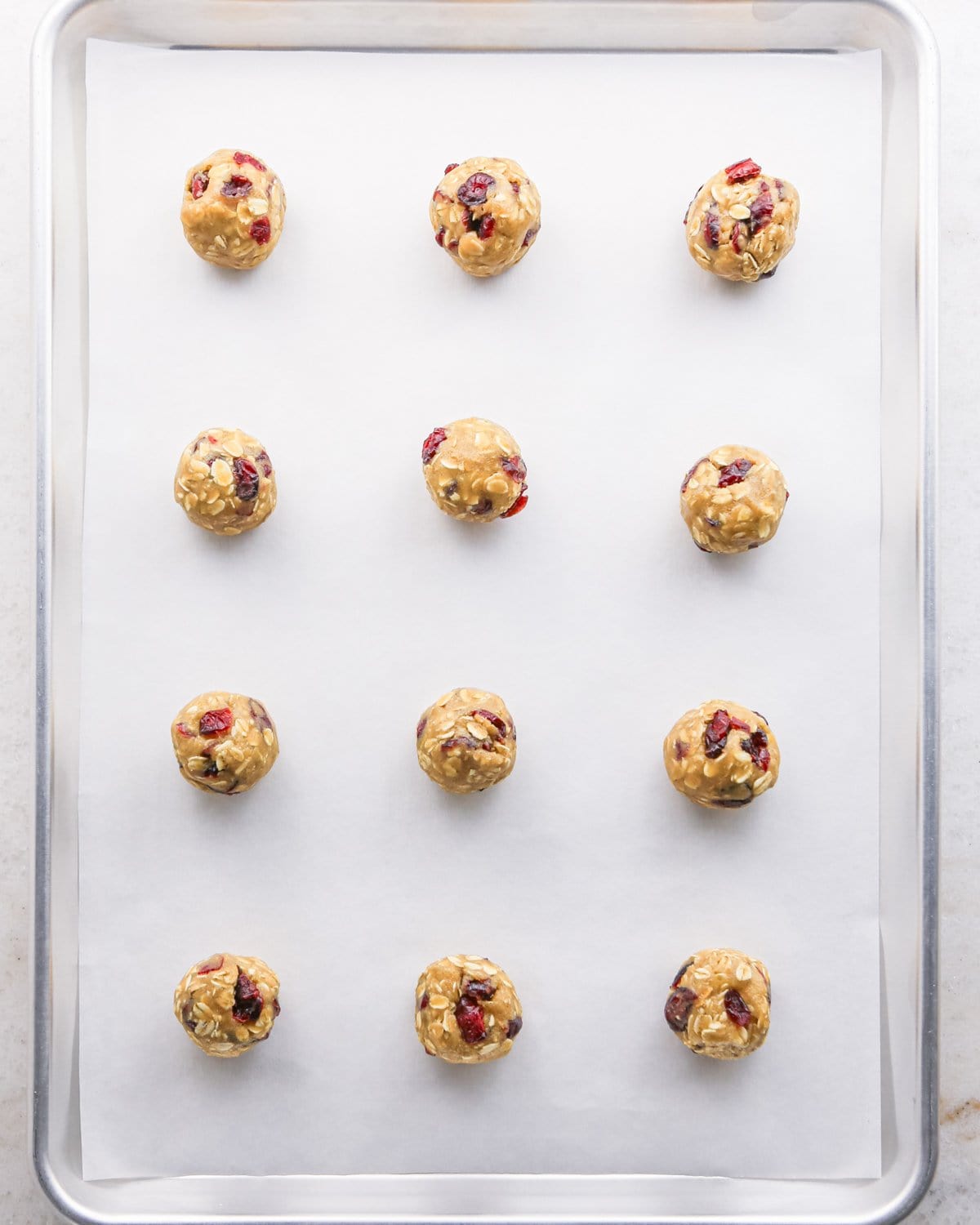 Making cranberry oatmeal cookies - overhead photo of 12 cranberry oatmeal cookie dough balls on a parchment-paper-covered baking sheet.
