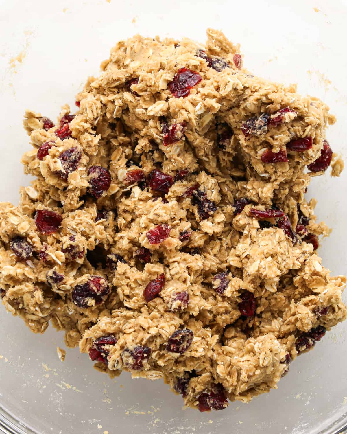 Making cranberry oatmeal cookies - overhead photo of dried cranberries being added to the cookie dough and mixed together.