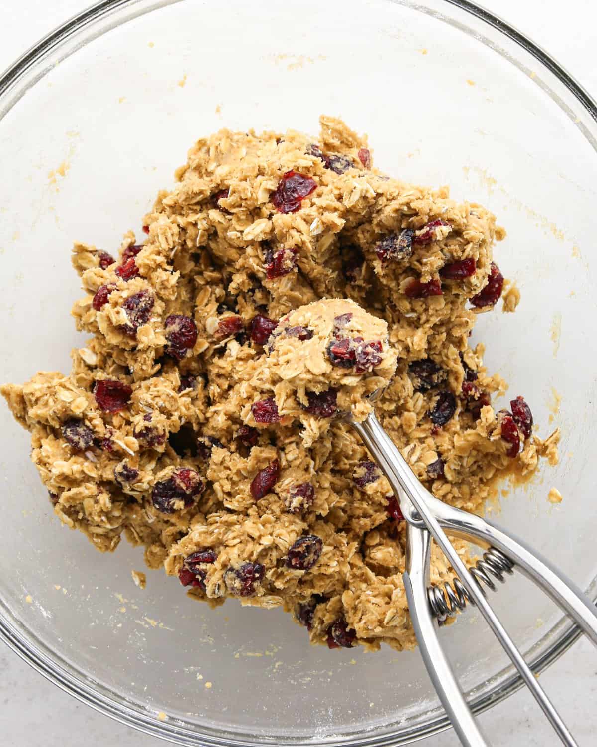 Making cranberry oatmeal cookies - overhead photo of a cookie scoop scooping out cookie dough from a clear bowl.
