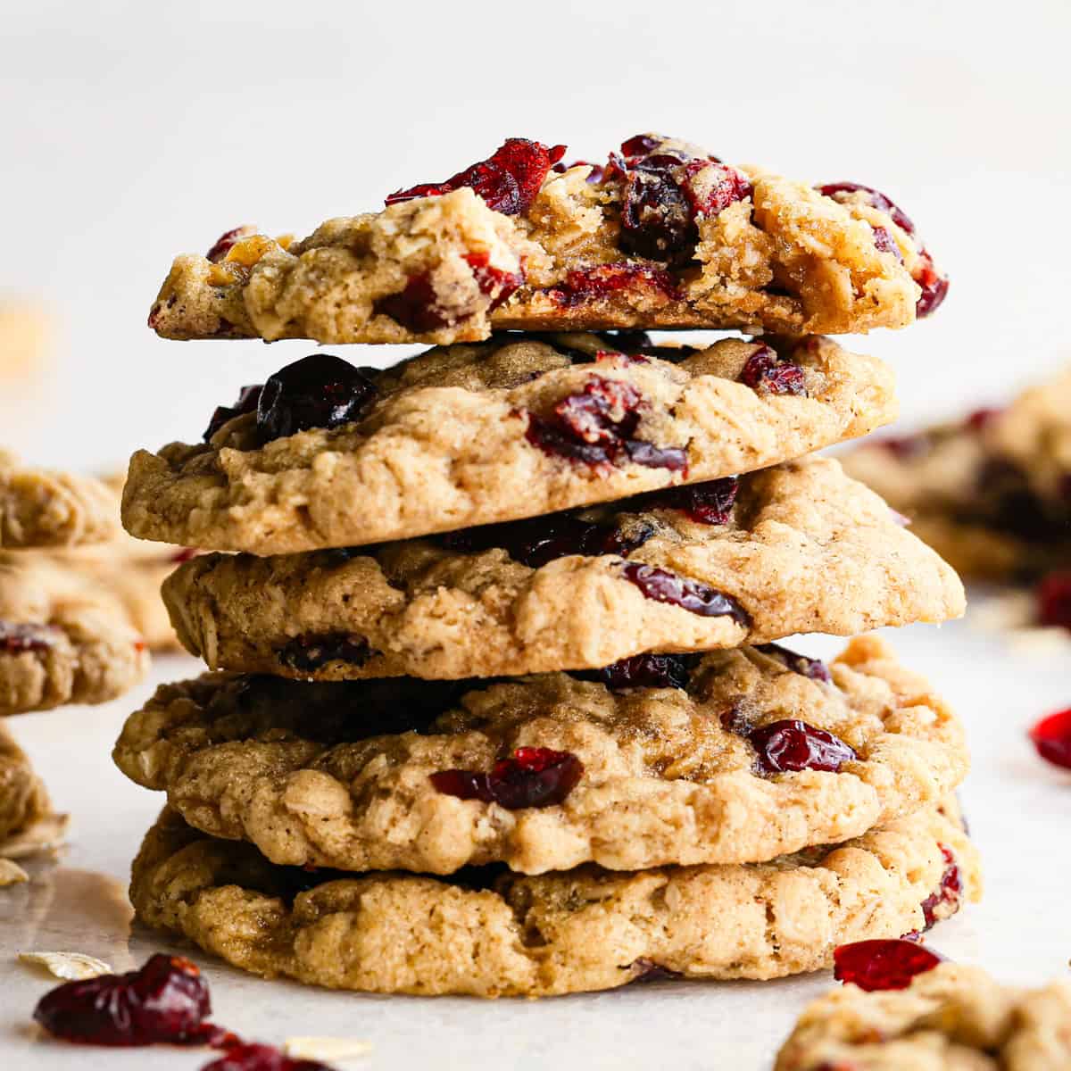 Stack of chewy cranberry oatmeal cookies, packed with oats and studded with dried cranberries, with the top cookie partially bitten to reveal its soft texture.