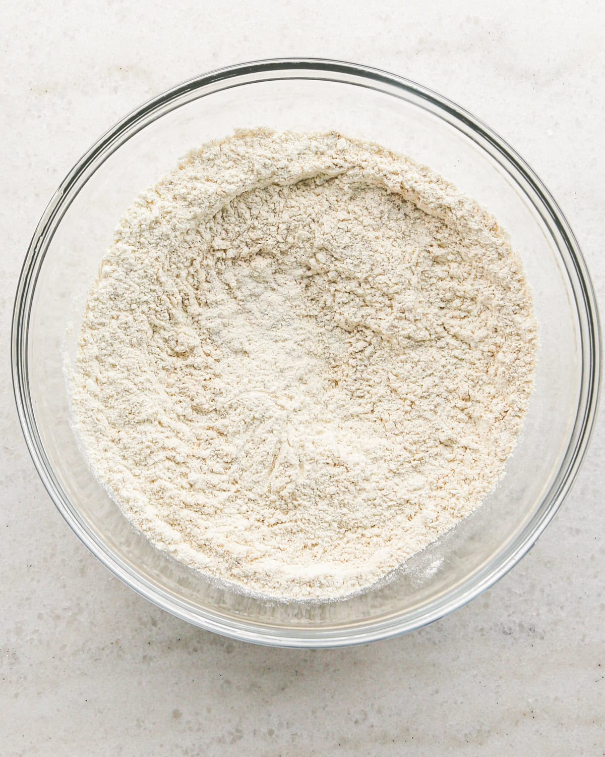 Making cranberry oatmeal cookies - overhead photo of dry ingredients in a clear mixing bowl and stirred together.