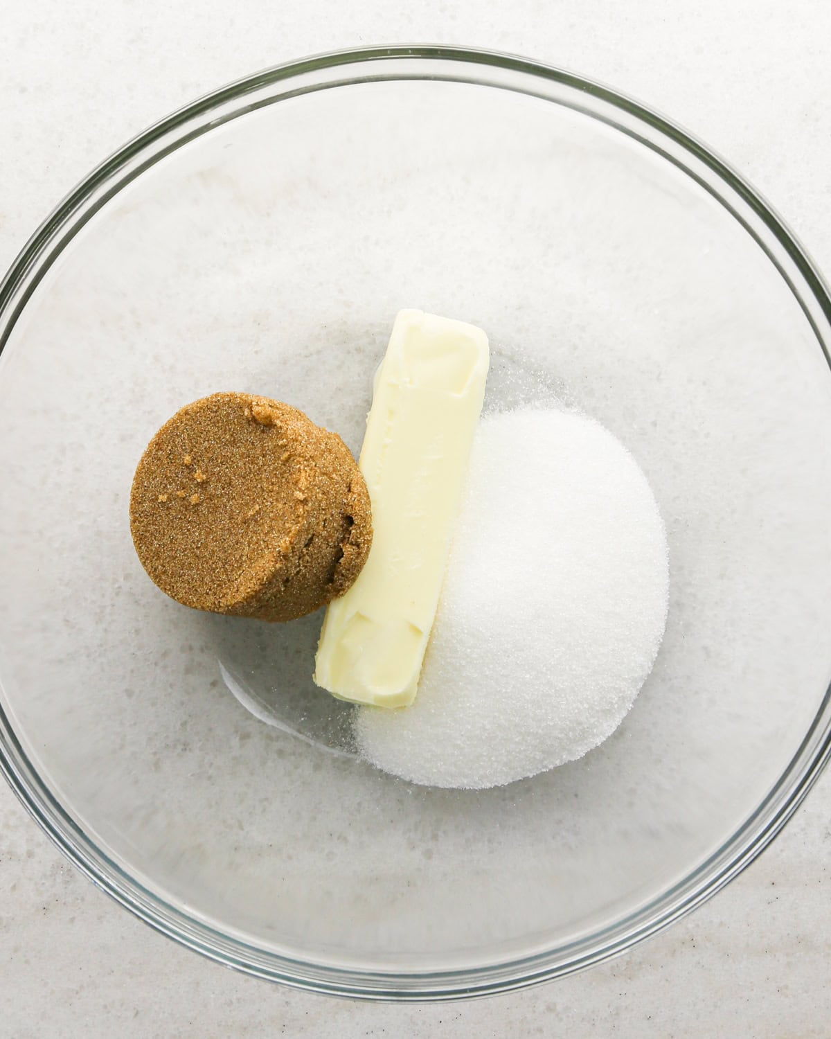 Making cranberry oatmeal cookies - overhead photo of butter, brown sugar, and sugar in a clear mixing bowl.