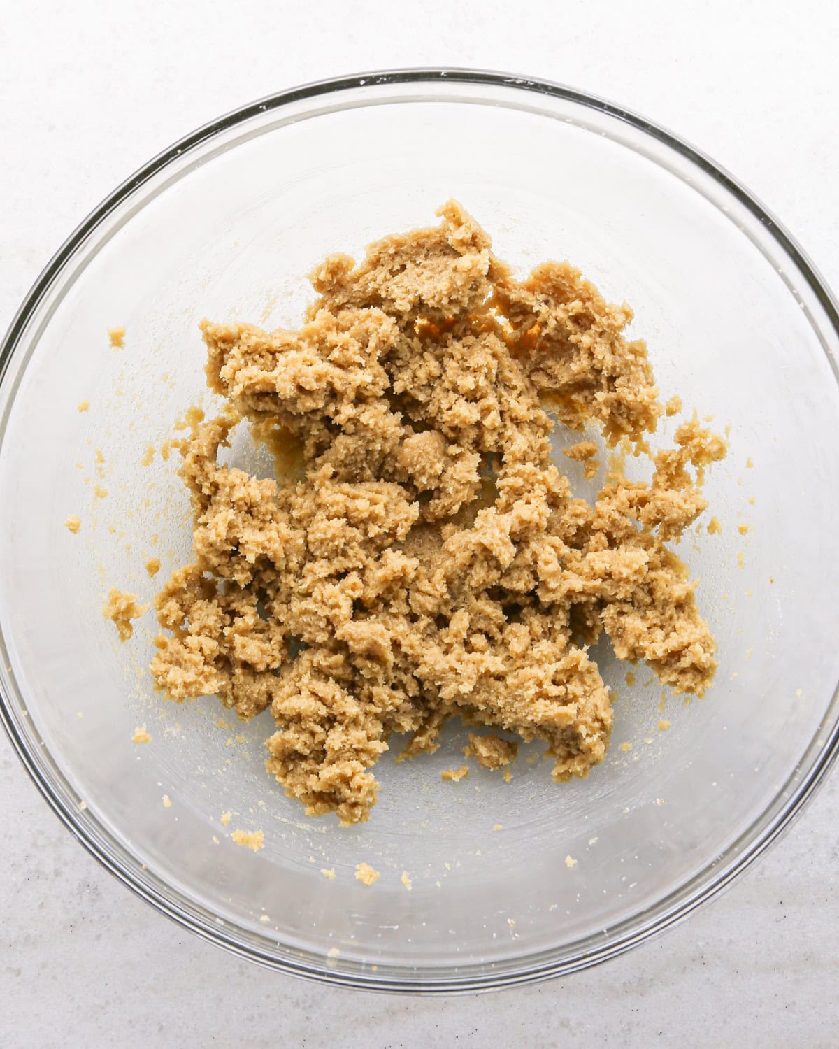 Making cranberry oatmeal cookies - overhead photo of butter, brown sugar, and sugar in a clear mixing bowl and mixed together.