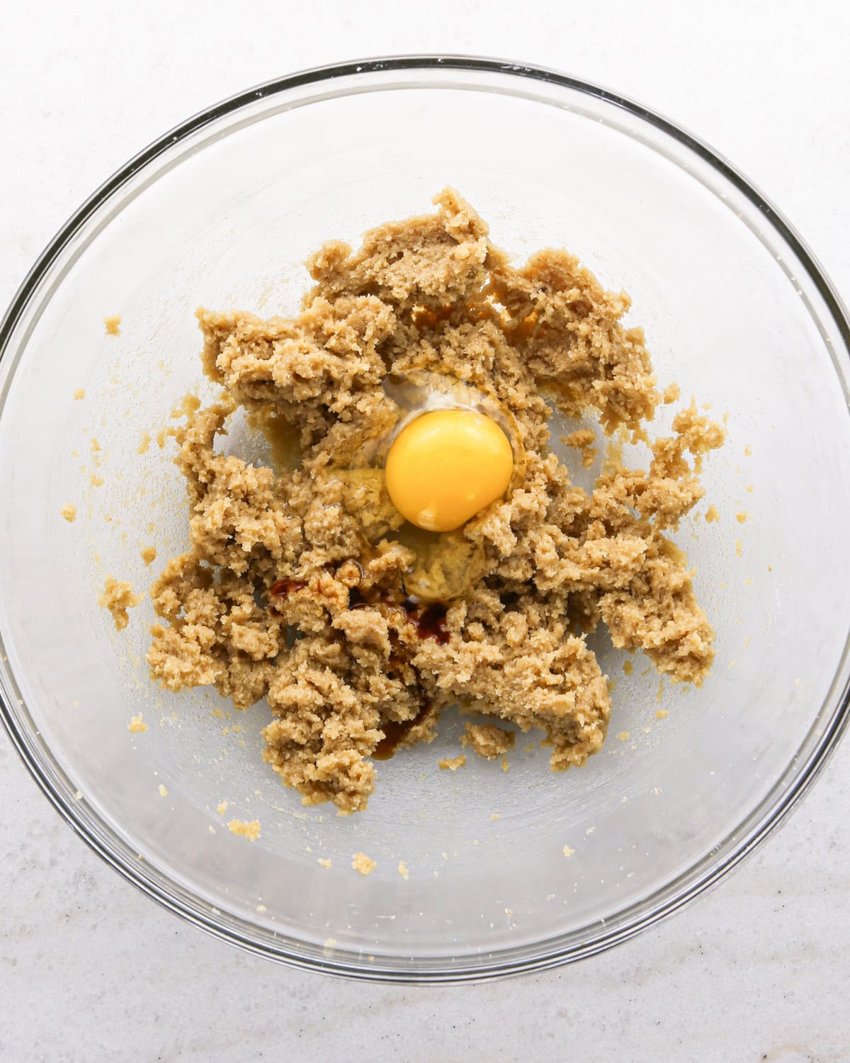 Making cranberry oatmeal cookies - overhead photo of butter, brown sugar, sugar, and an egg in a clear mixing bowl.