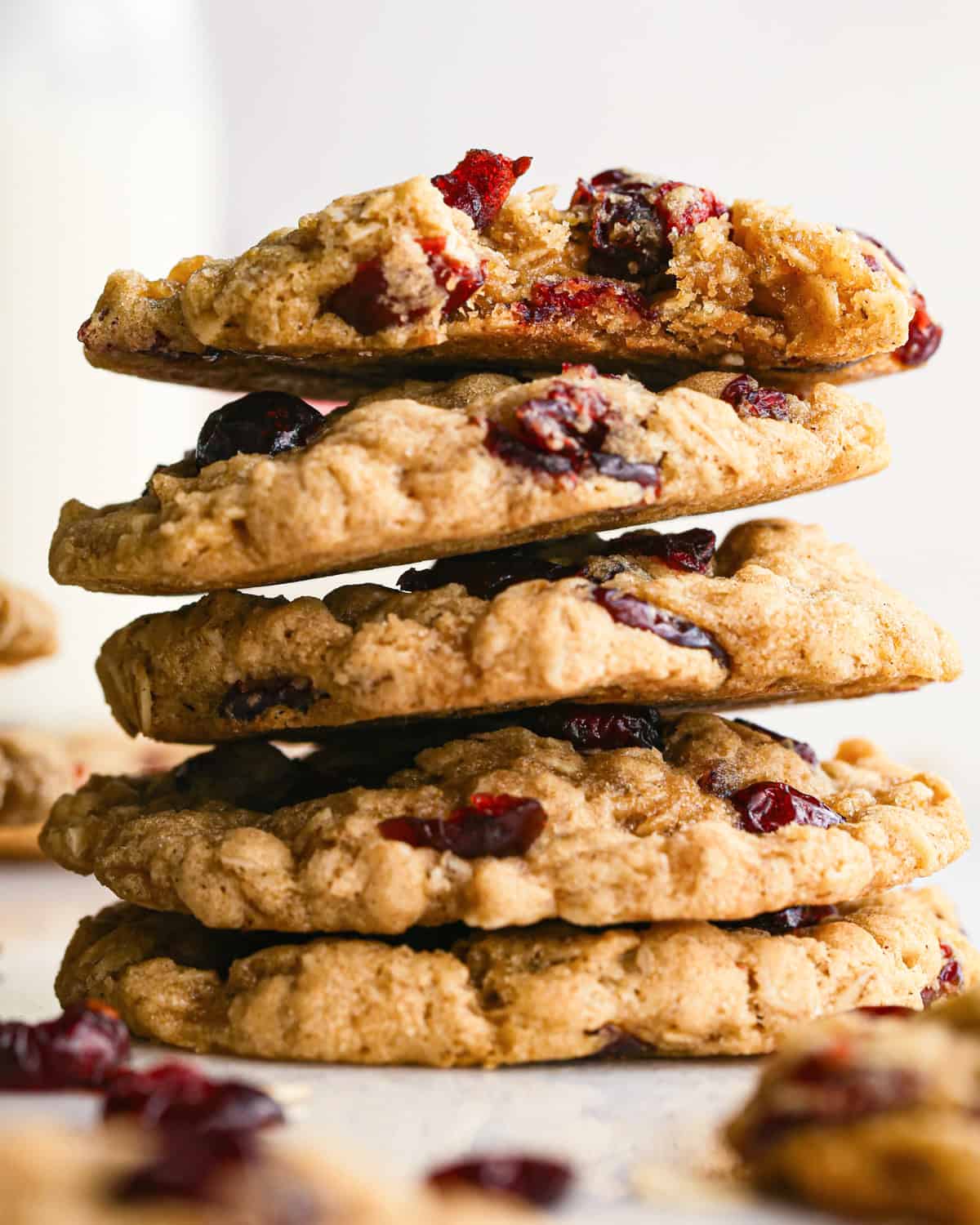 Close-up photo of a stack of cranberry oatmeal cookies on a countertop ready to serve, a bite is taken out of the top cookie.