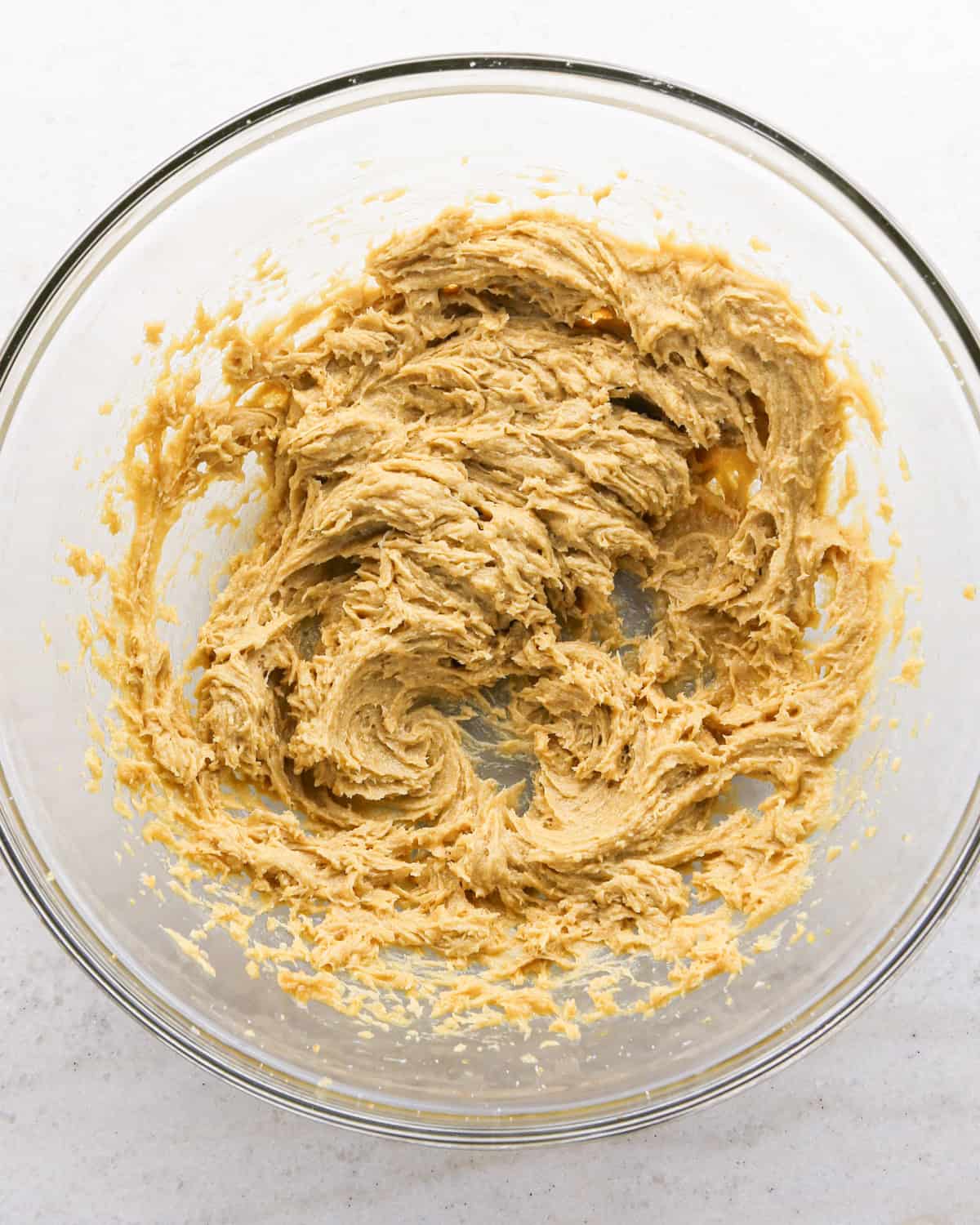 Making cranberry oatmeal cookies - overhead photo of butter, brown sugar, sugar, and an egg in a clear mixing bowl and mixed together.