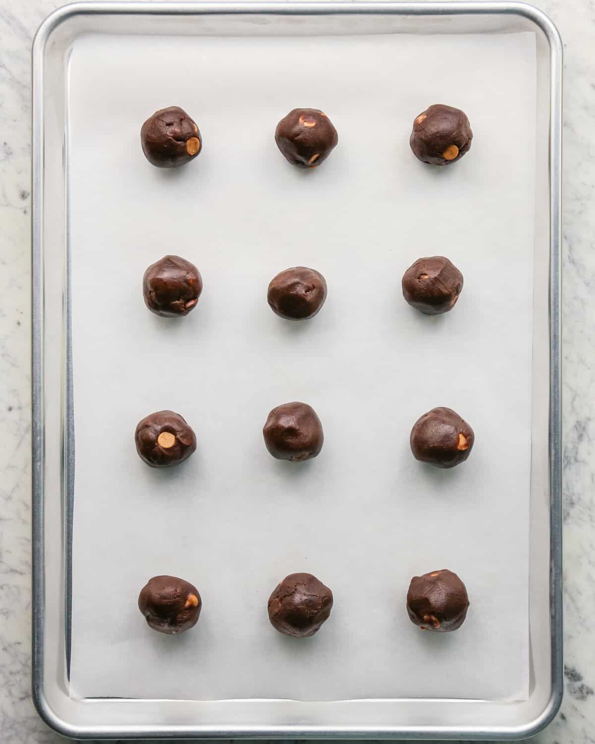 Overhead photo of a baking sheet topped with parchment paper, with 12 balls of raw cookie dough on top.