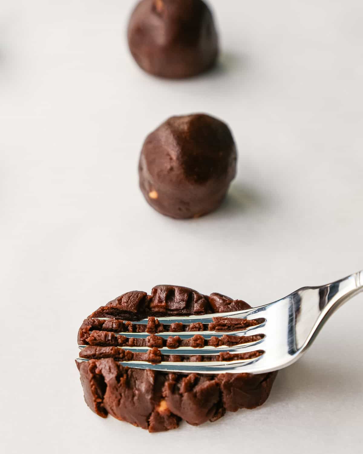 Making peanut butter chip cookies - a silver fork presses down on a ball of cookie dough. 