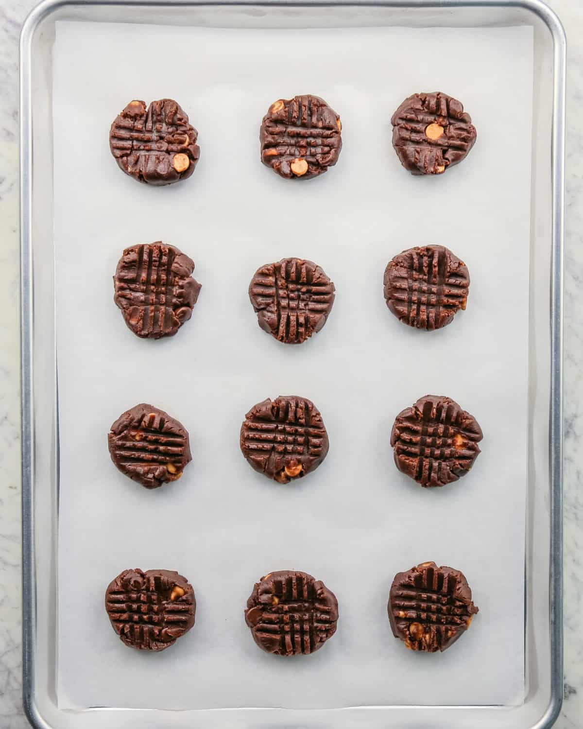 Overhead photo of 12 pre-baked cookies on a baking sheet, with fork imprints on each one.