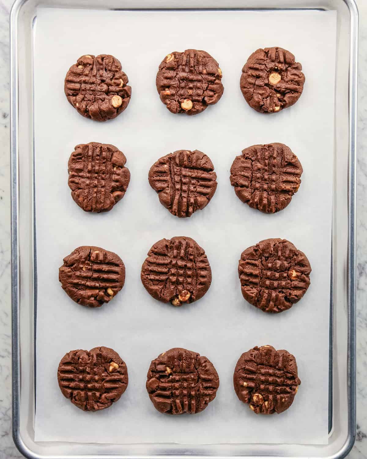 Overhead photo of 12 pre-baked cookies on a baking sheet, with fork imprints on each one.