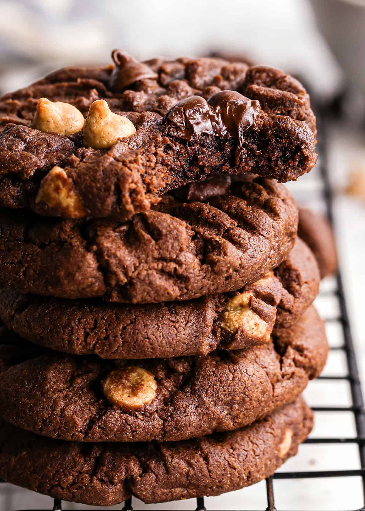 Close up photo of a stack of 5 chocolate peanut butter chip cookies with one cookie partially eaten on top.