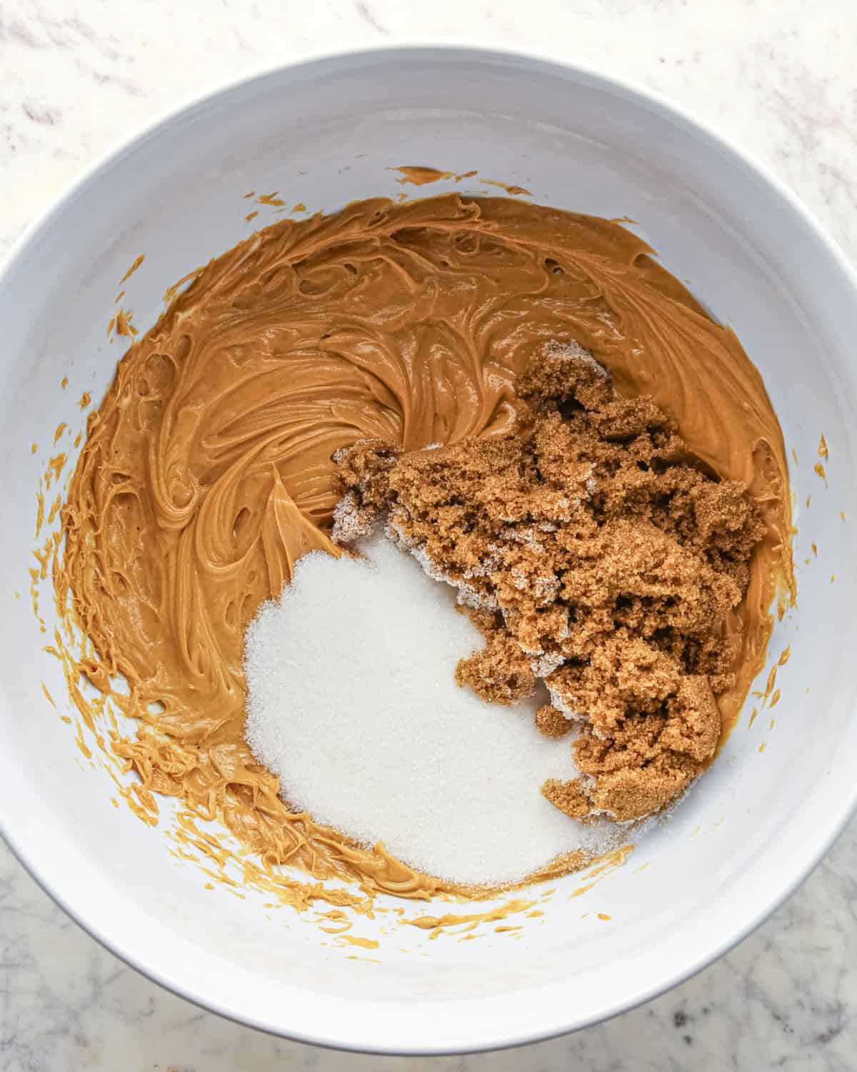 Making chocolate peanut butter chip cookies - butter, peanut butter, sugar, and brown sugar in a white bowl.
