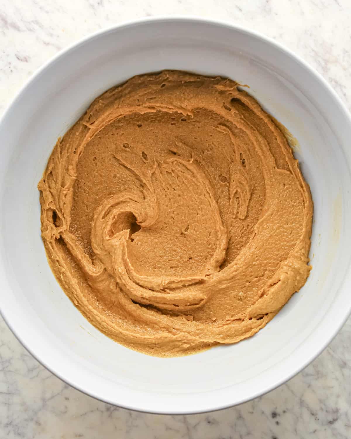 Making chocolate peanut butter chip cookies - butter, peanut butter, sugar, and brown sugar are mixed together in a white bowl.