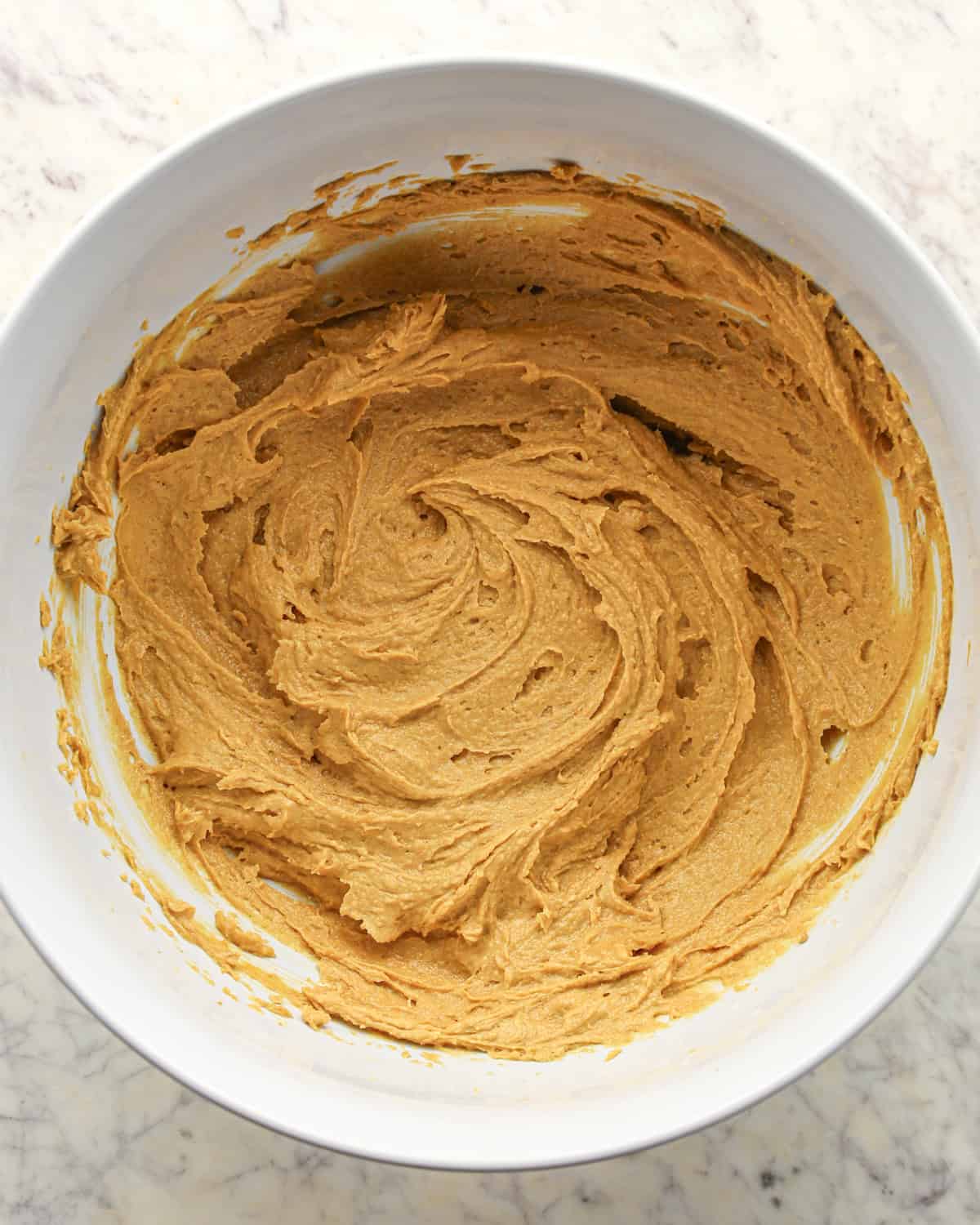 Making chocolate peanut butter chip cookies - vanilla, egg, milk, butter, peanut butter, sugar, and brown sugar mixed together in a white bowl.