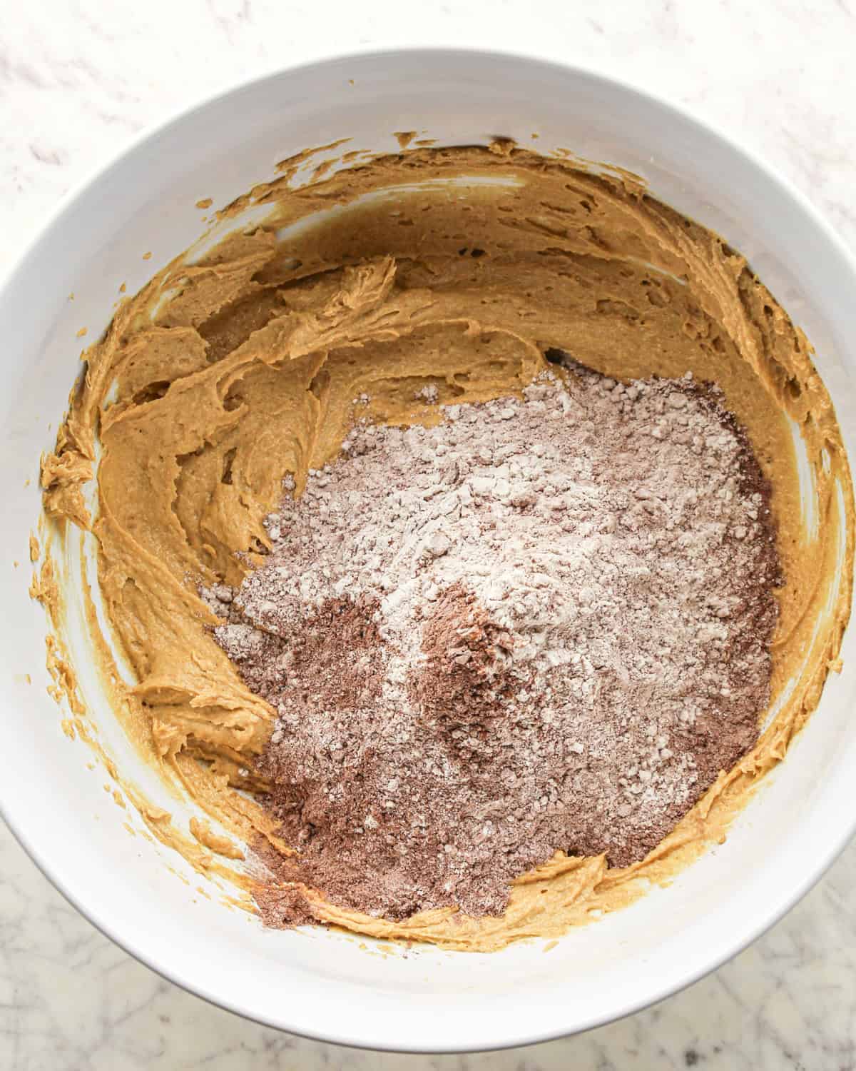 Making chocolate peanut butter chip cookies - dry ingredients and wet ingredients placed together in a white bowl.